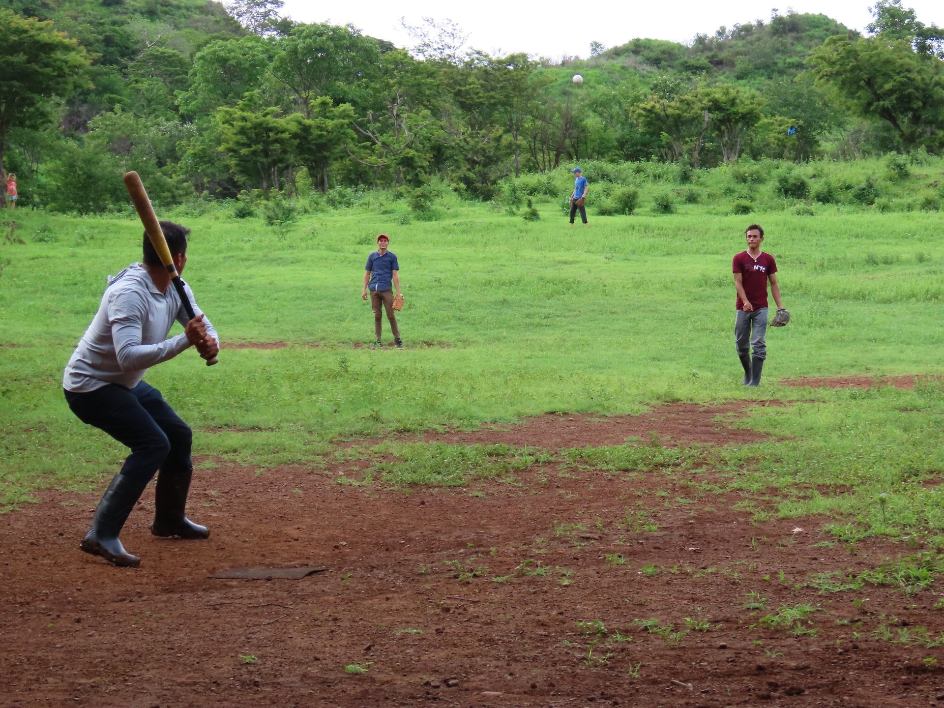 A group of young men playing baseball in a rural countryside.