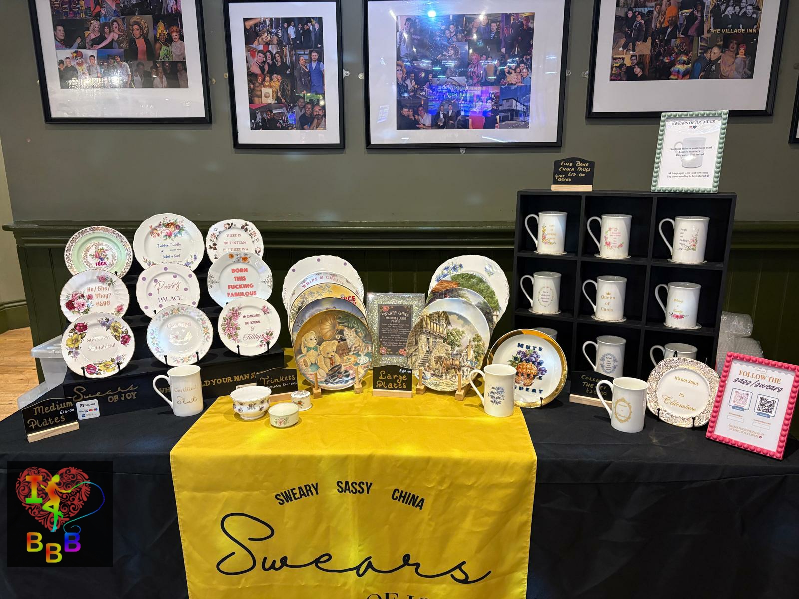 A display of Swears of Joy sassy china plates and mugs with humorous, sweary messages on a yellow tablecloth.