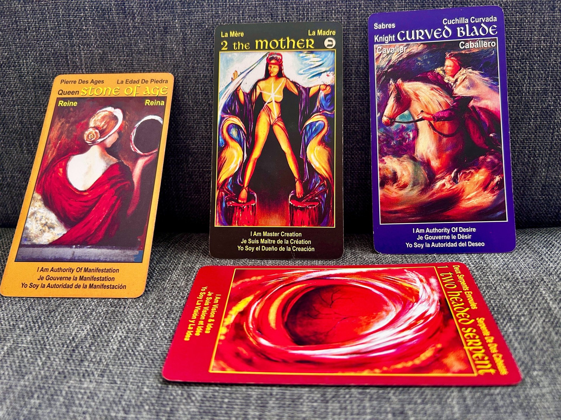 Four colorful tarot cards with mystical artwork displayed on a grey fabric surface.