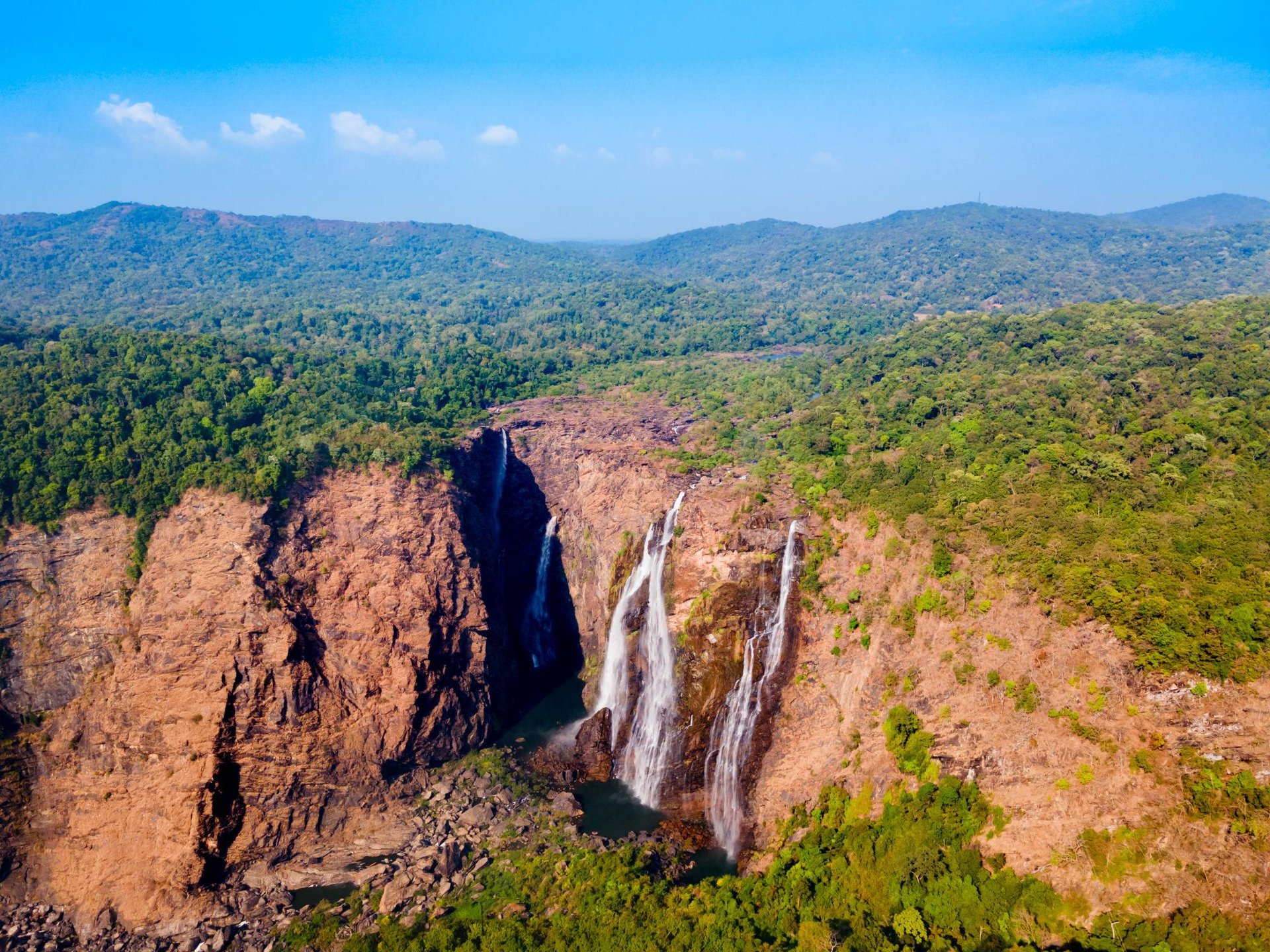 Aerial view of Jog Falls cascading down rocky cliffs surrounded by lush green tropical forests in Karnataka.