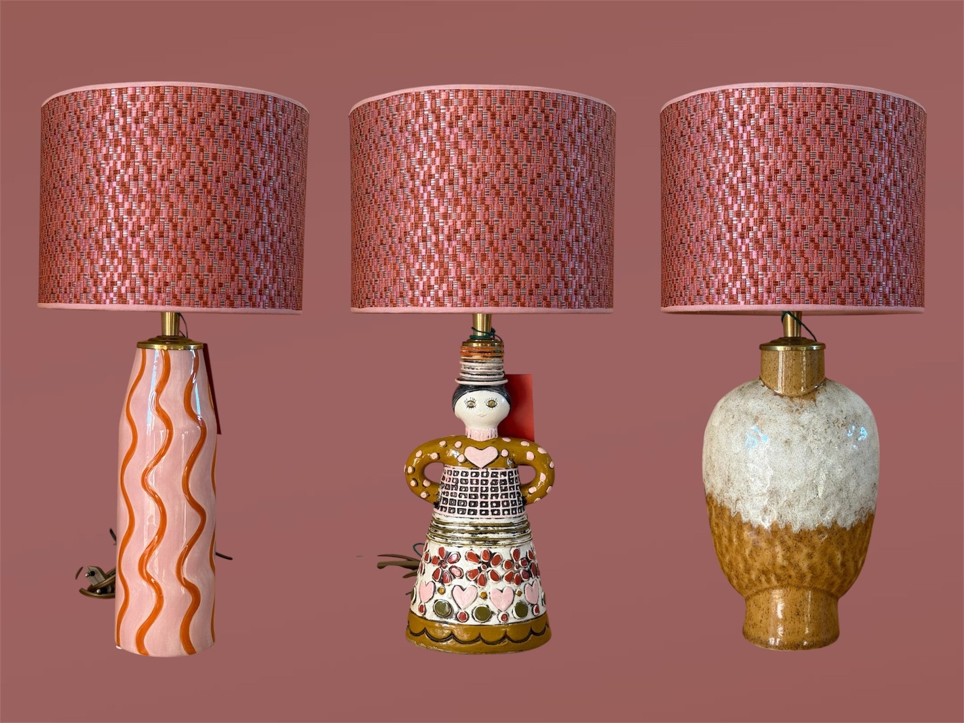 Three unique mid-century modern ceramic table lamps with pink patterned lampshades on a mauve background.