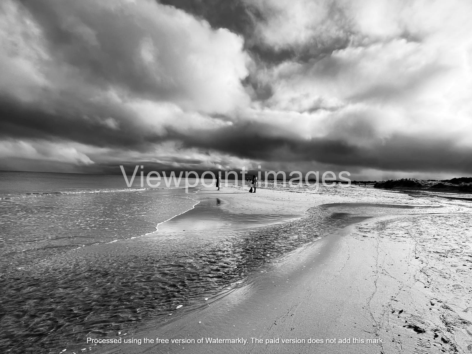 Dramatic black and white landscape of a sandy beach with dark storm clouds reflecting on the ocean tide.