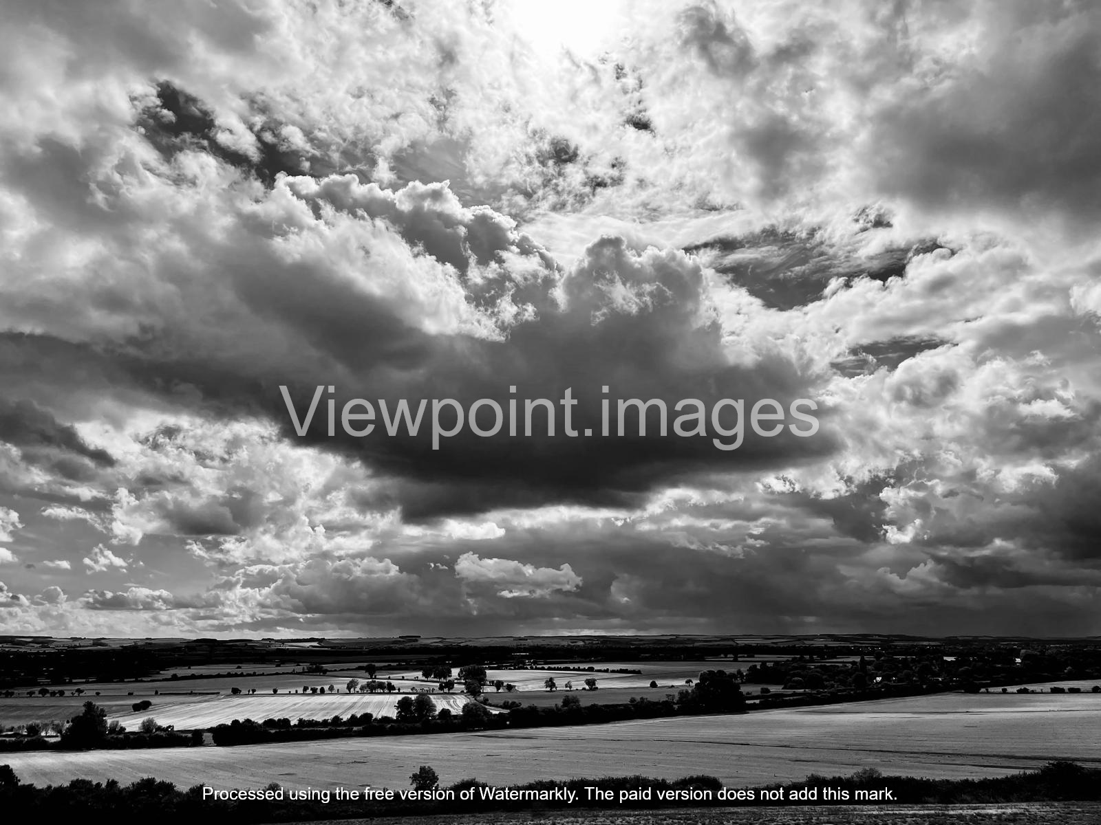 Dramatic black and white landscape of storm clouds over rural farmland and fields.