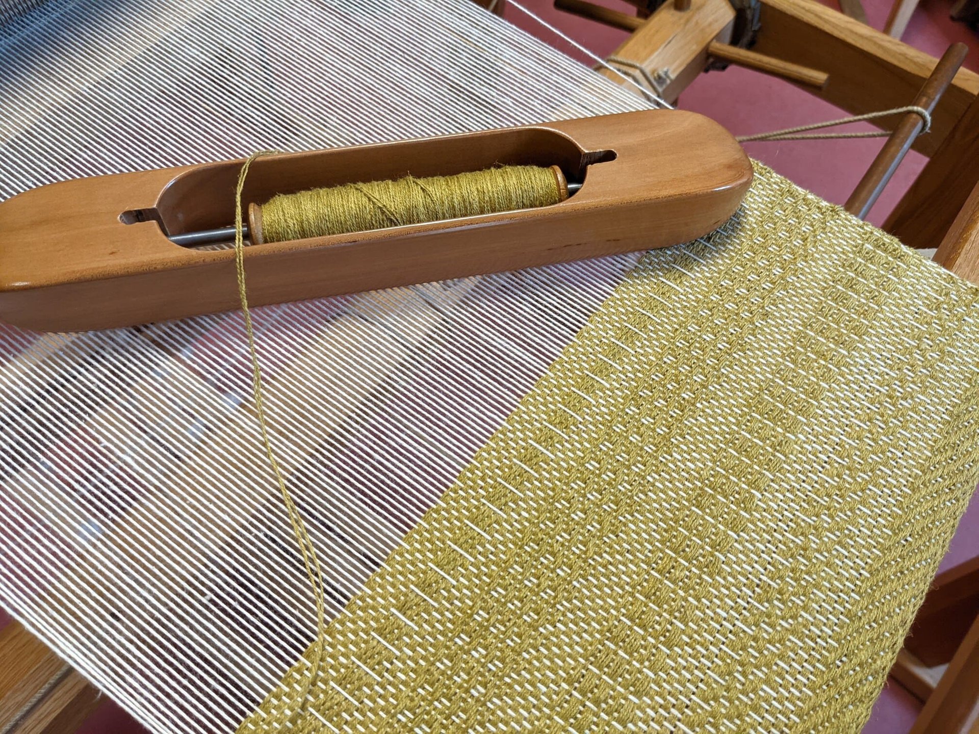 a weaving loom with shuttle and olive green threads on a 4 harness textile in progress