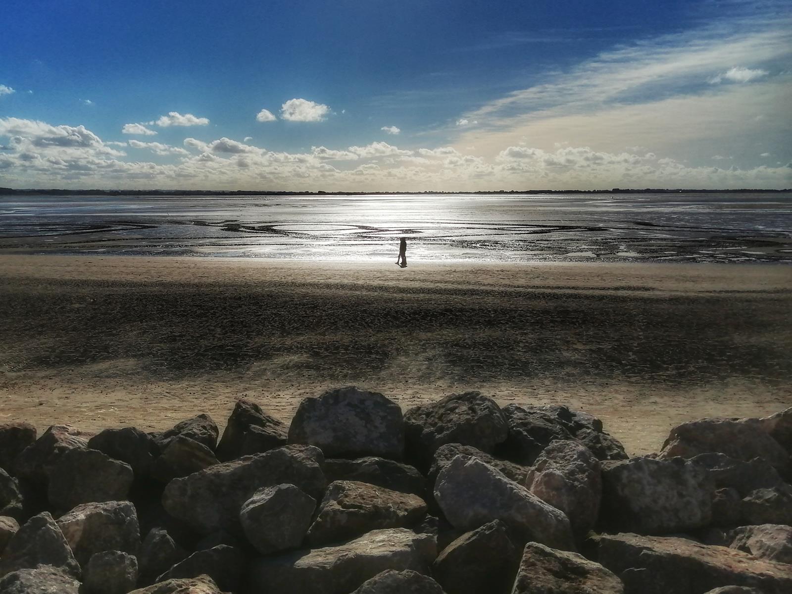 une personne debout sur une plage avec des rochers et la mer au coucher de soleil 