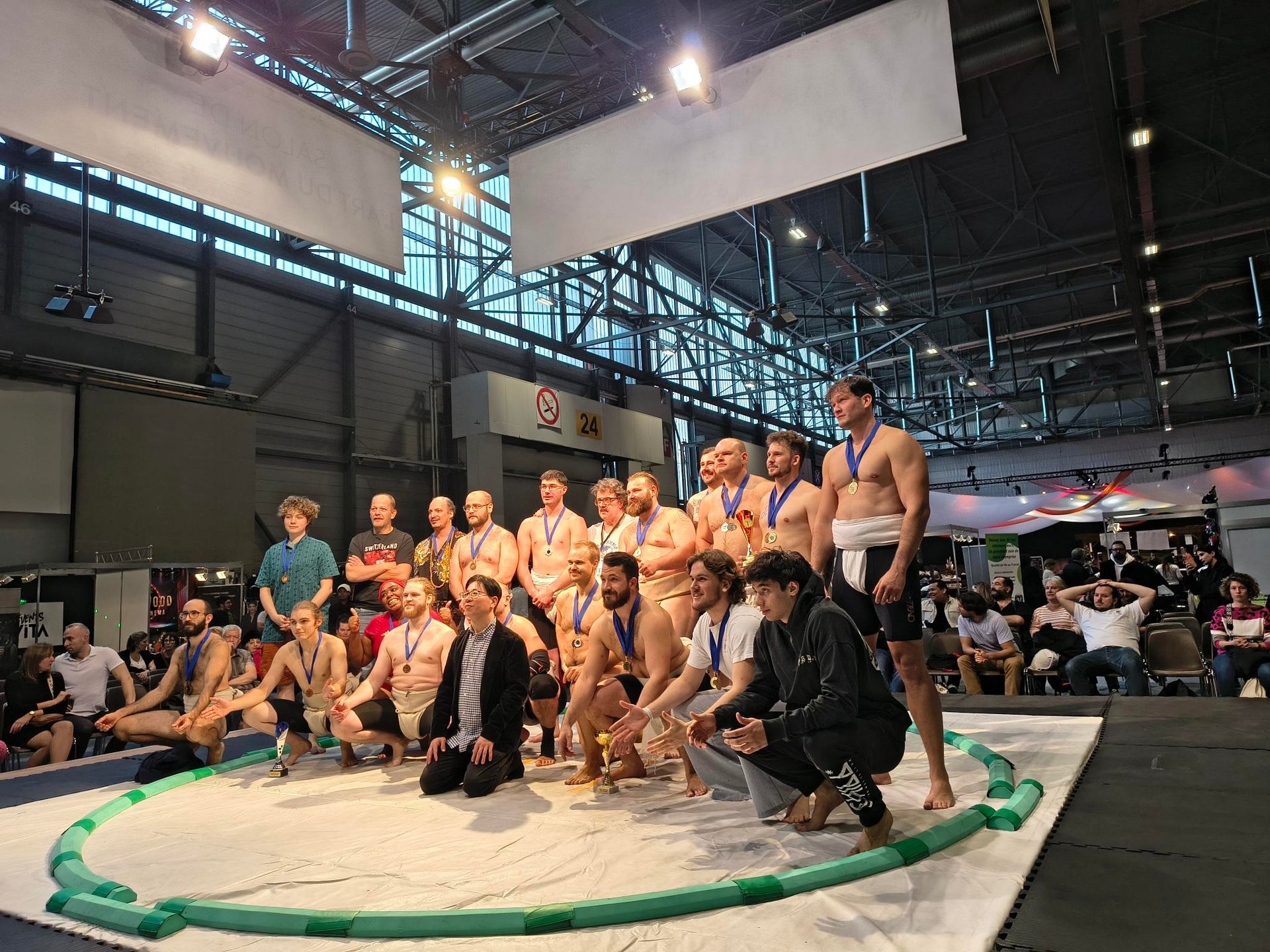 21 hommes et femmes prenant la pose sur un dohyo de Sumo