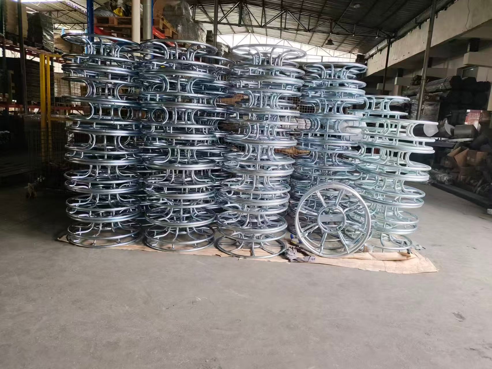 Stacks of industrial galvanized steel metal hose reels in a manufacturing warehouse facility.