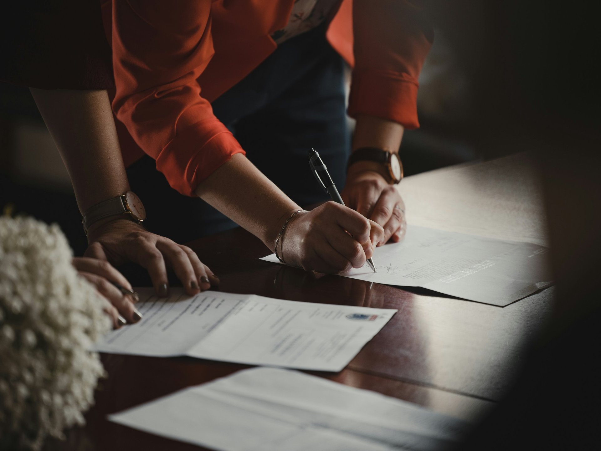 Professional person in an orange blazer signing a legal contract or business document with a pen.