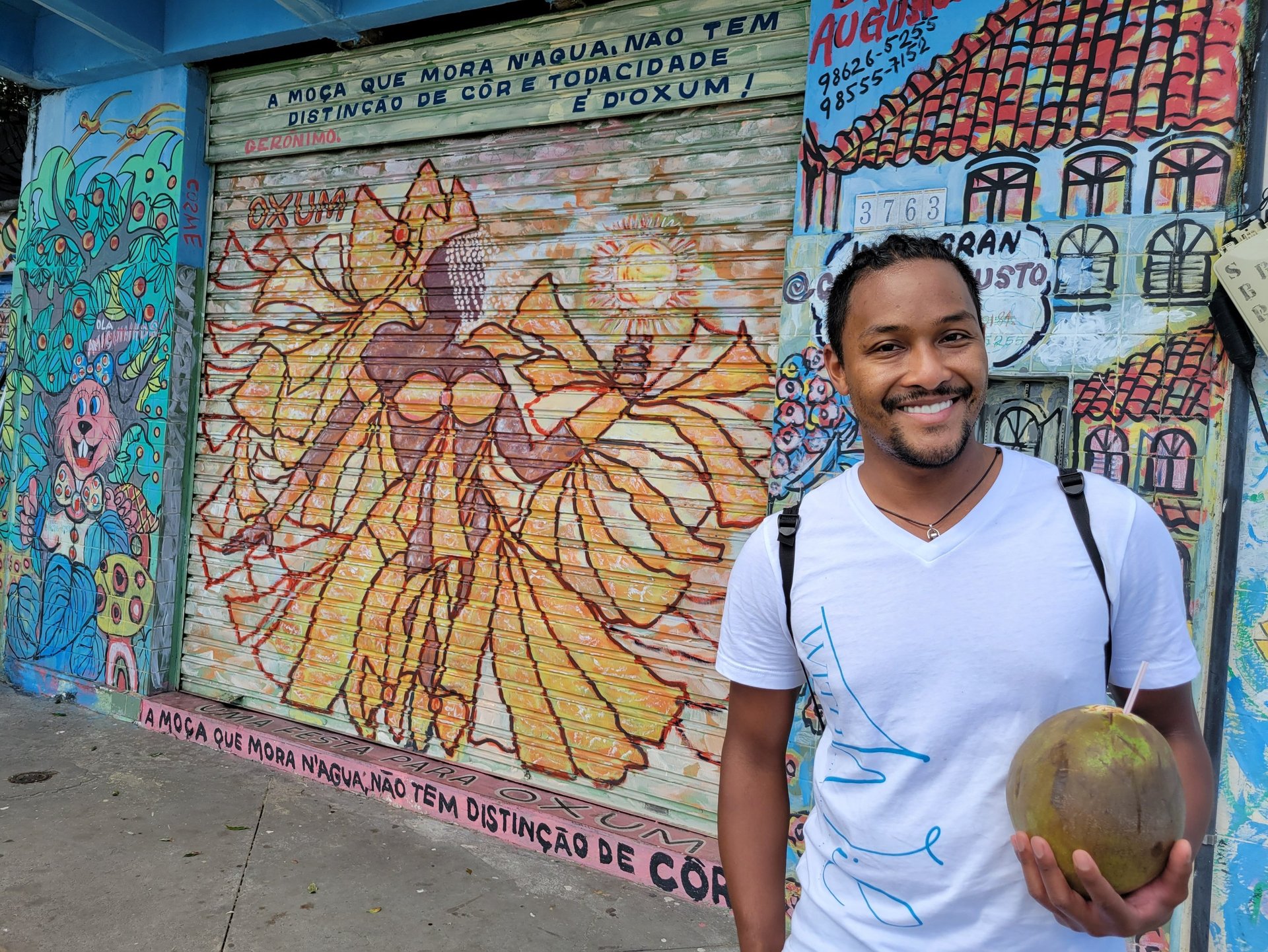 Wil smiling with a coconut in hand in Salvador in front of a drawing of Oshun
