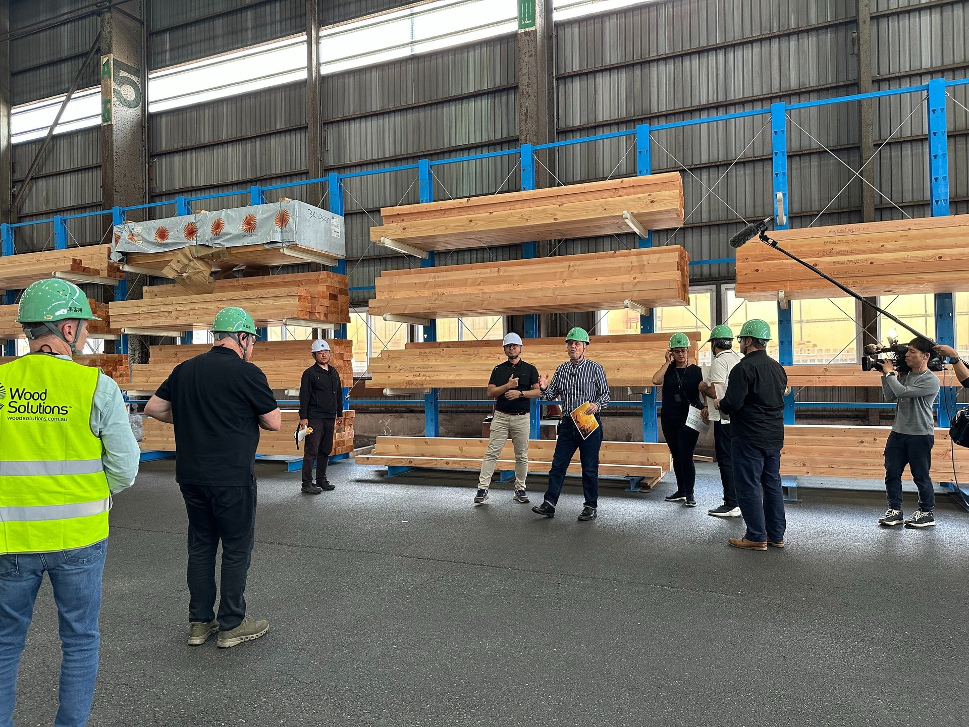 A group of engineers in hard hats film a site tour of a mass timber warehouse facility with glulam beams.