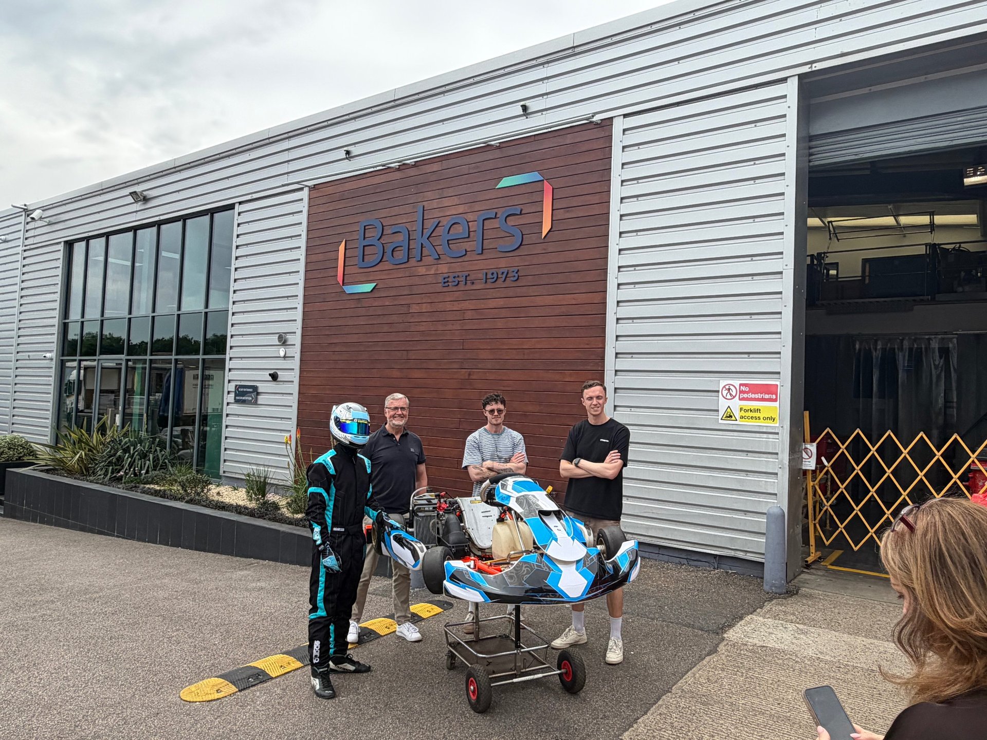 A group of people posing with Burwood Motorsports racing kart outside Bakers Labels factory