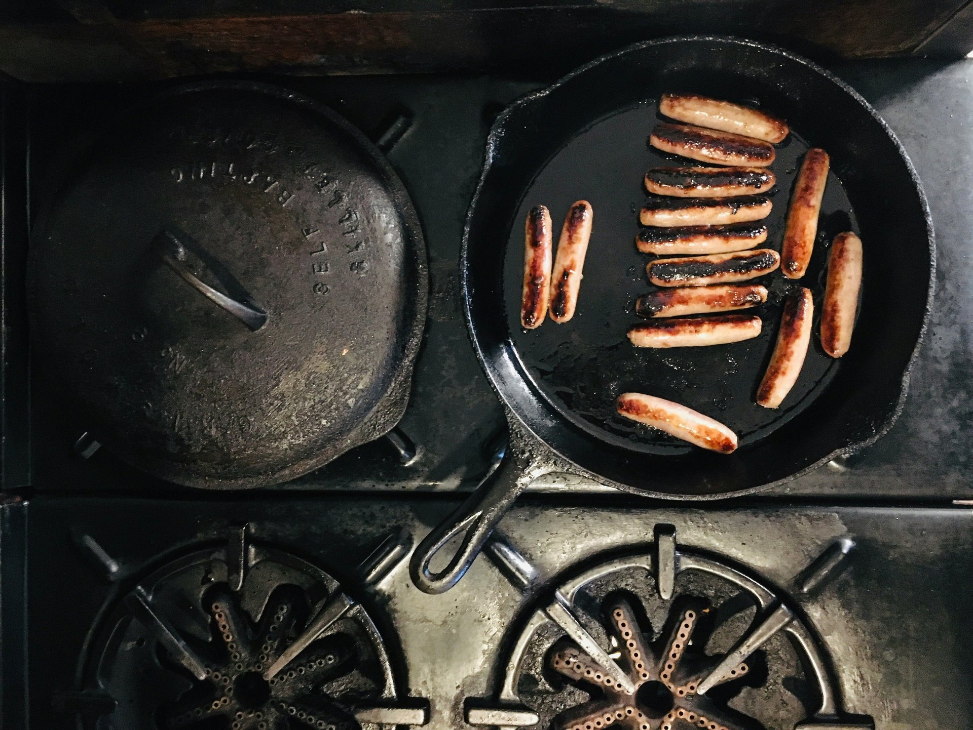 Breakfast sausage links browning in a seasoned cast iron skillet on a vintage gas stove.