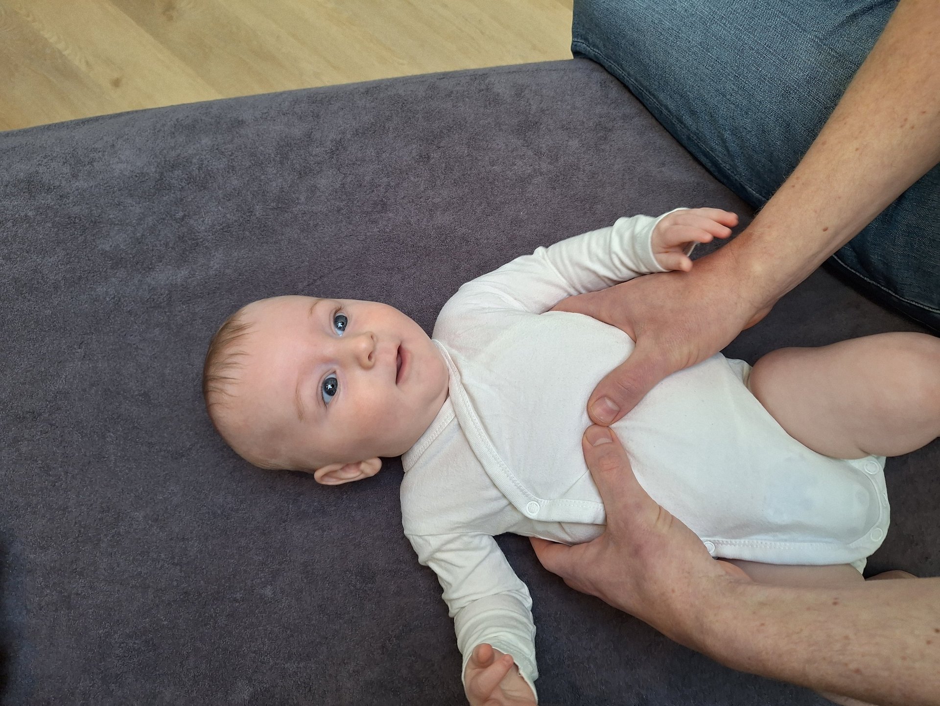 een baby ligt op een tafel met 2 handen van een man