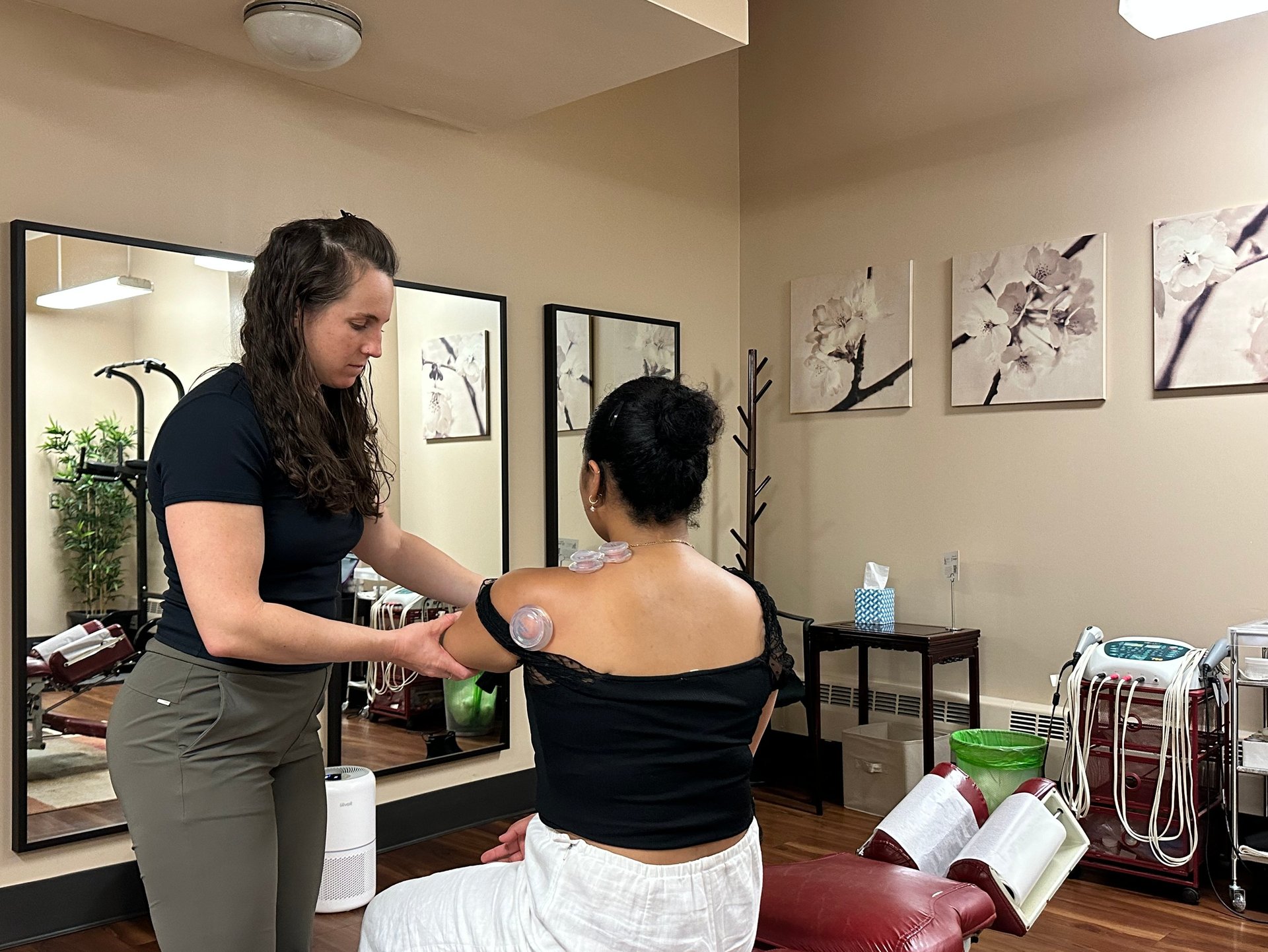 Chiropractor cupping a patient's shoulder and assisting movement with treatment room in background. 