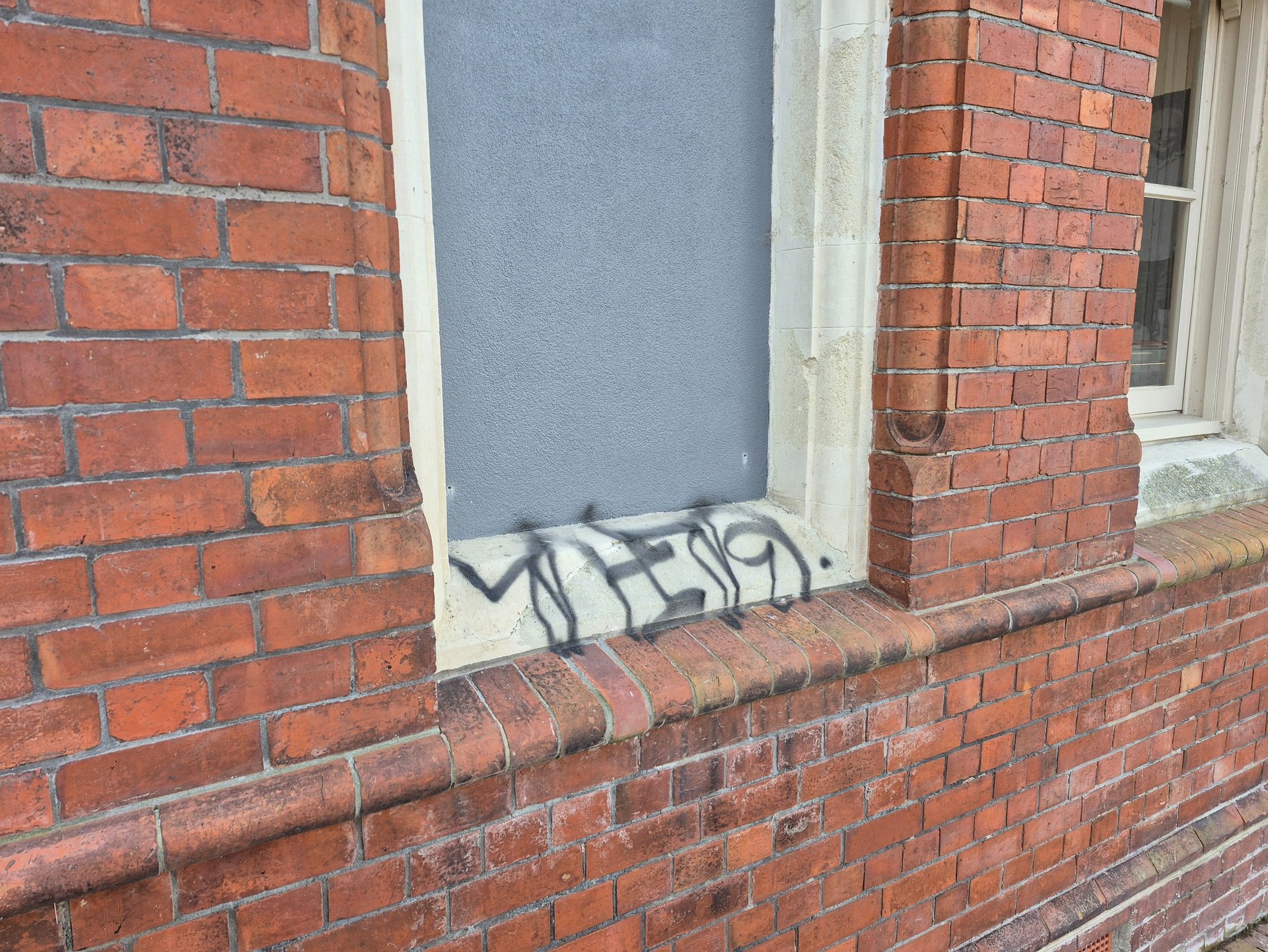 Black spray paint graffiti tag on the stone ledge of a red brick building window.