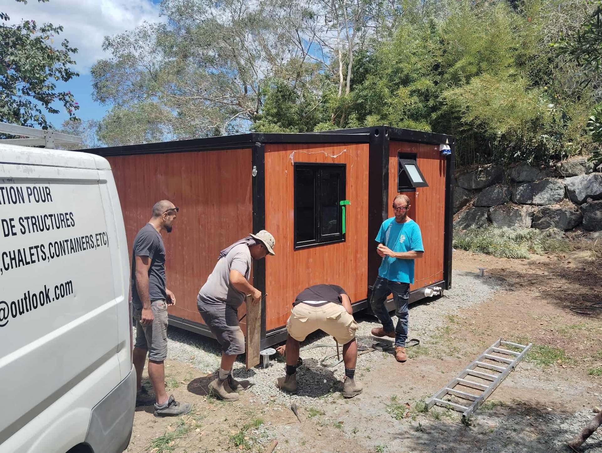 Ouvriers installant un conteneur habitable sur un terrain en gravier.