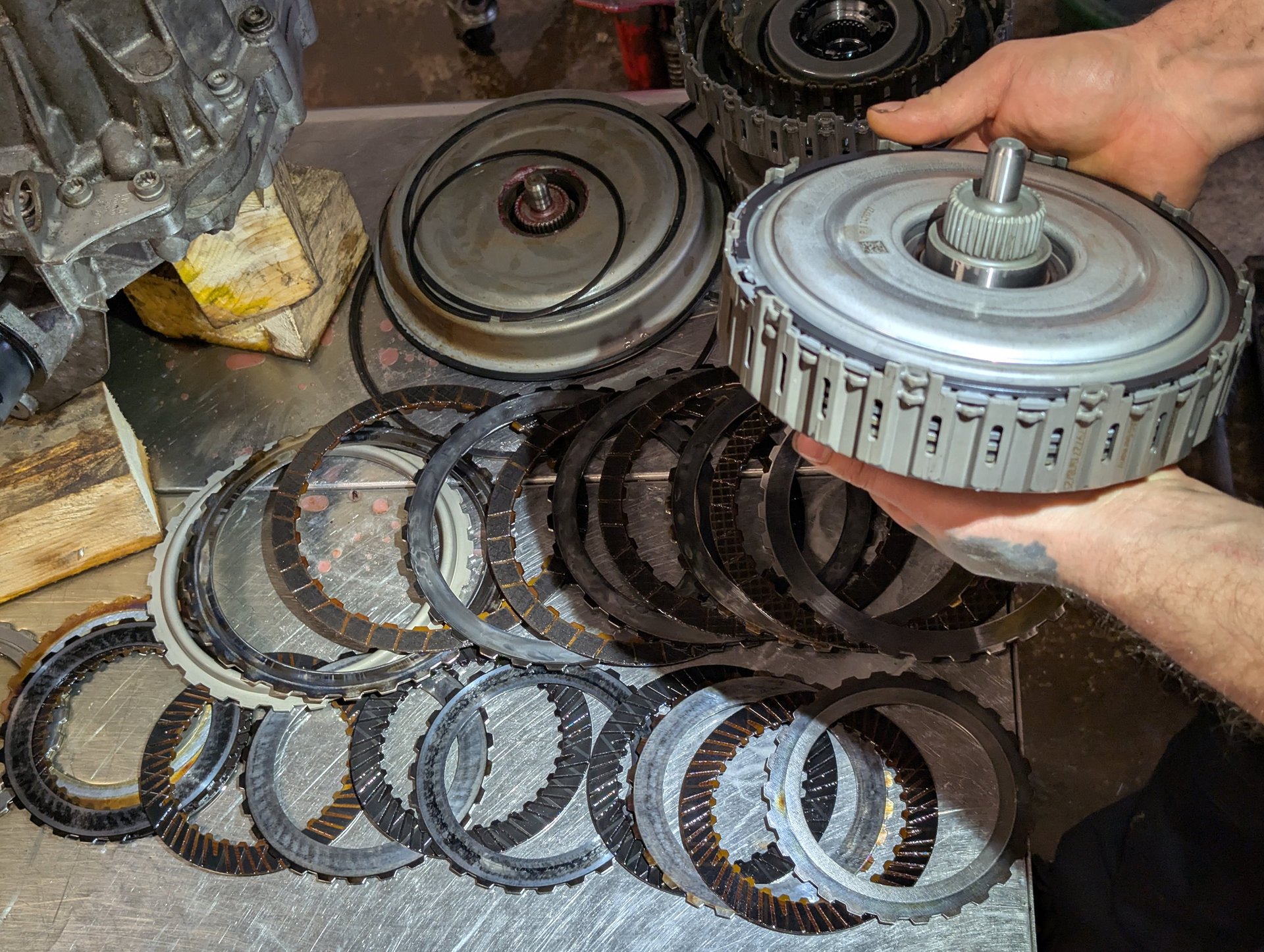 A mechanic holding a dual clutch assembly over a set of metal friction discs on a workbench.