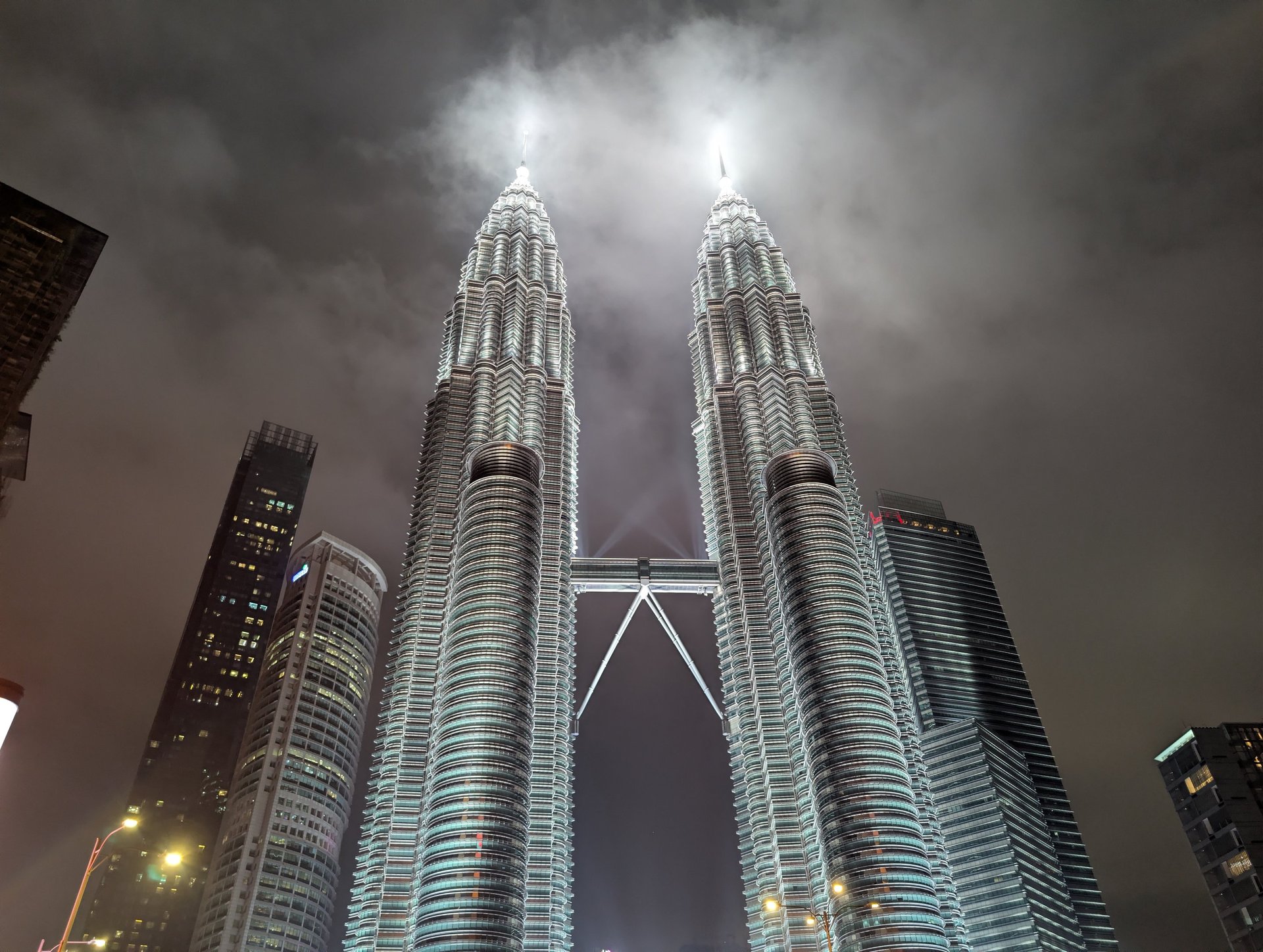 Illuminated Petronas Twin Towers in Kuala Lumpur, Malaysia, at night under a cloudy sky.