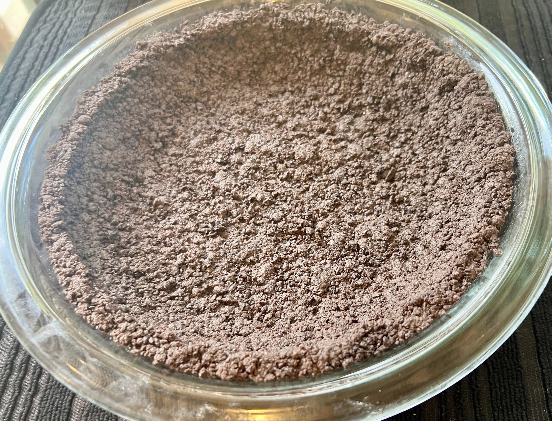 Homemade chocolate cookie pie crust pressed into a clear glass baking dish.