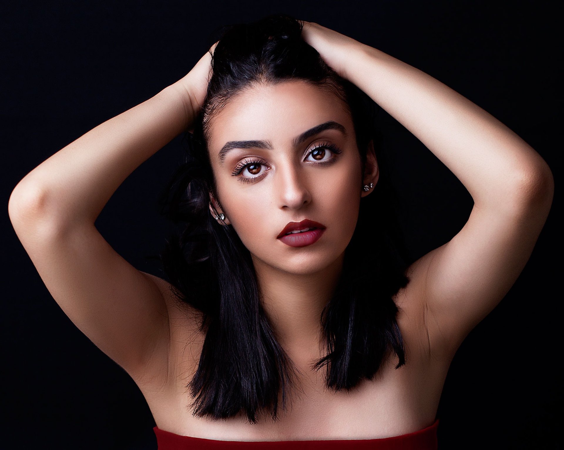 a beautiful brown eyed girl with tanned skin, plump auburn lips, pulling her hair back and posing like a model