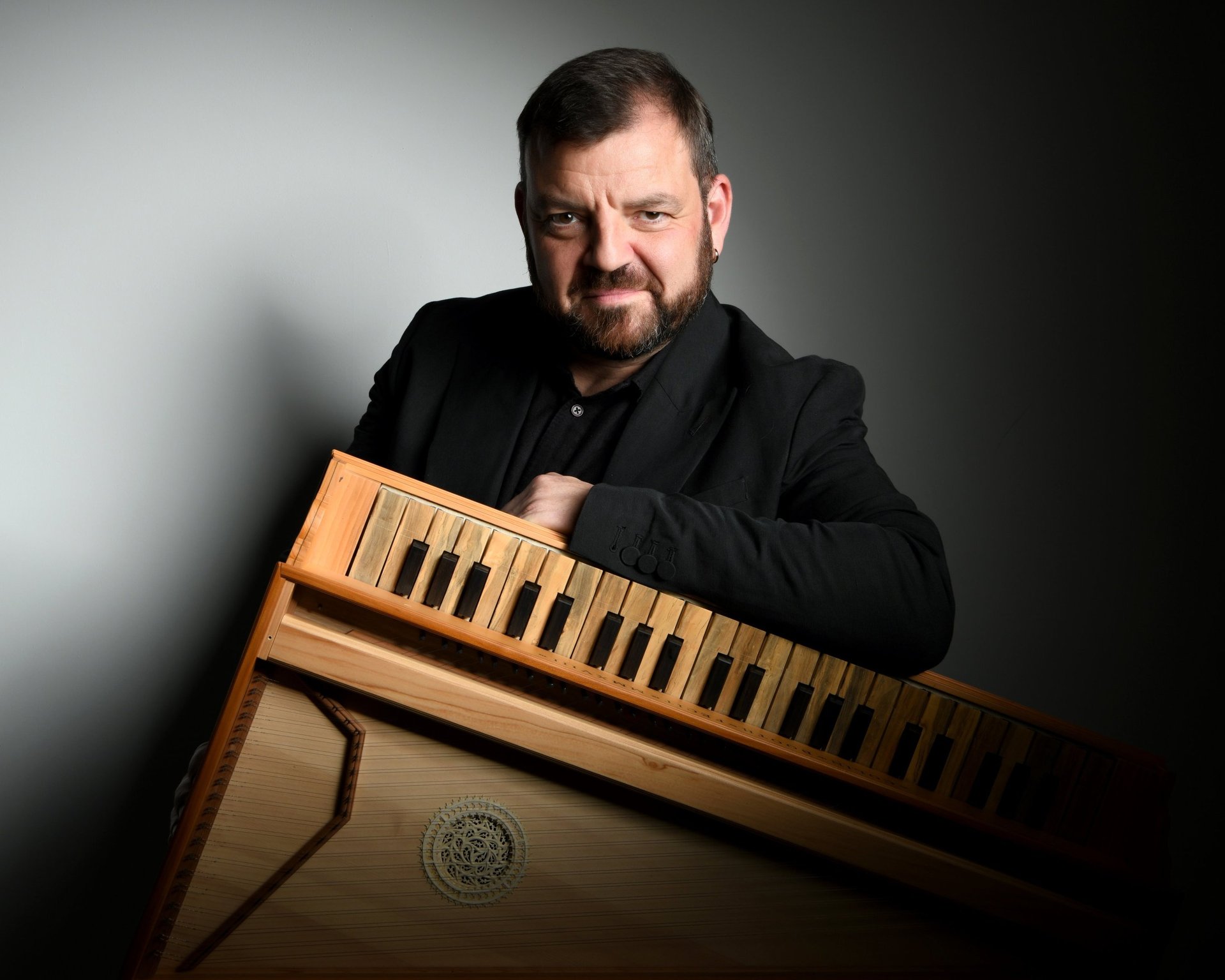 Steven Devine portrait looking at the camera with left arm resting on a musical instrument