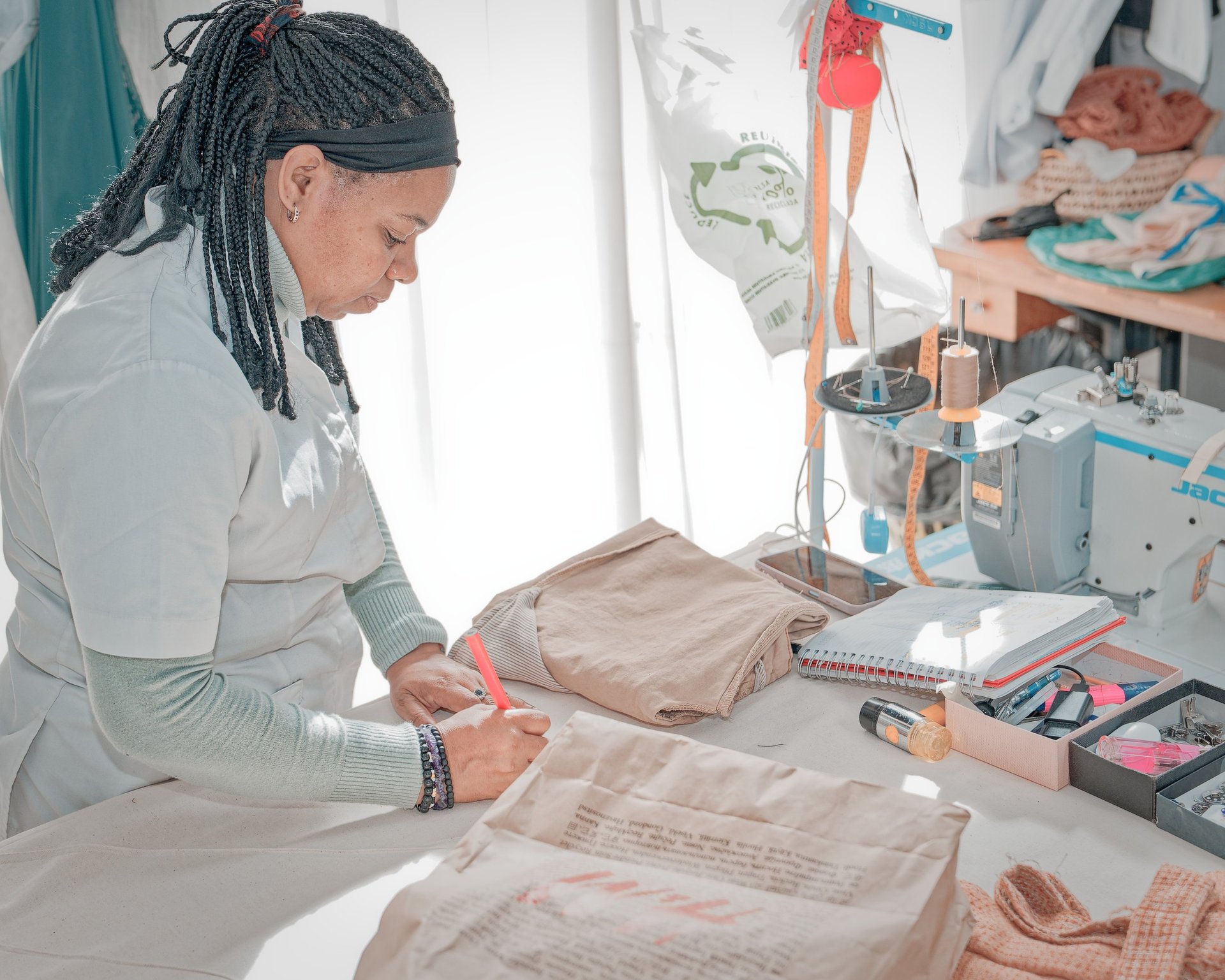 Modista trabajando en un taller de costura, marcando una prenda doblada sobre la mesa junto a una má