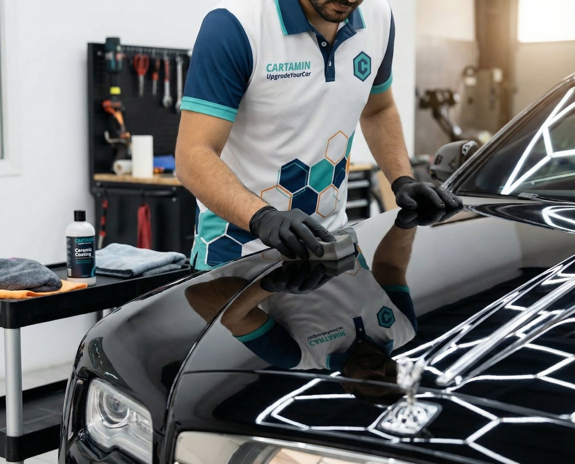 Professional applying protective ceramic coating to a luxury black car hood with a sponge.