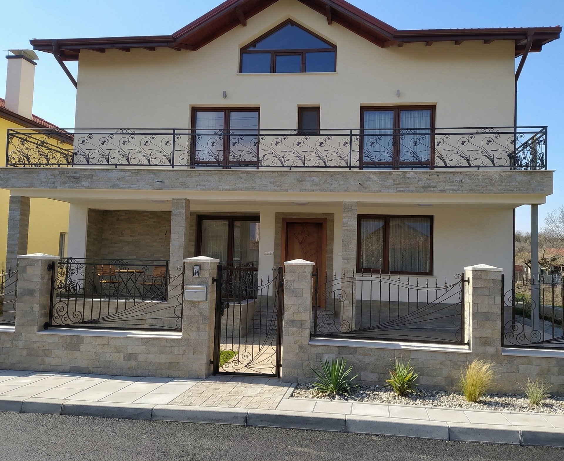 Modern two-story house with elegant wrought iron balcony railings and a matching stone garden fence.