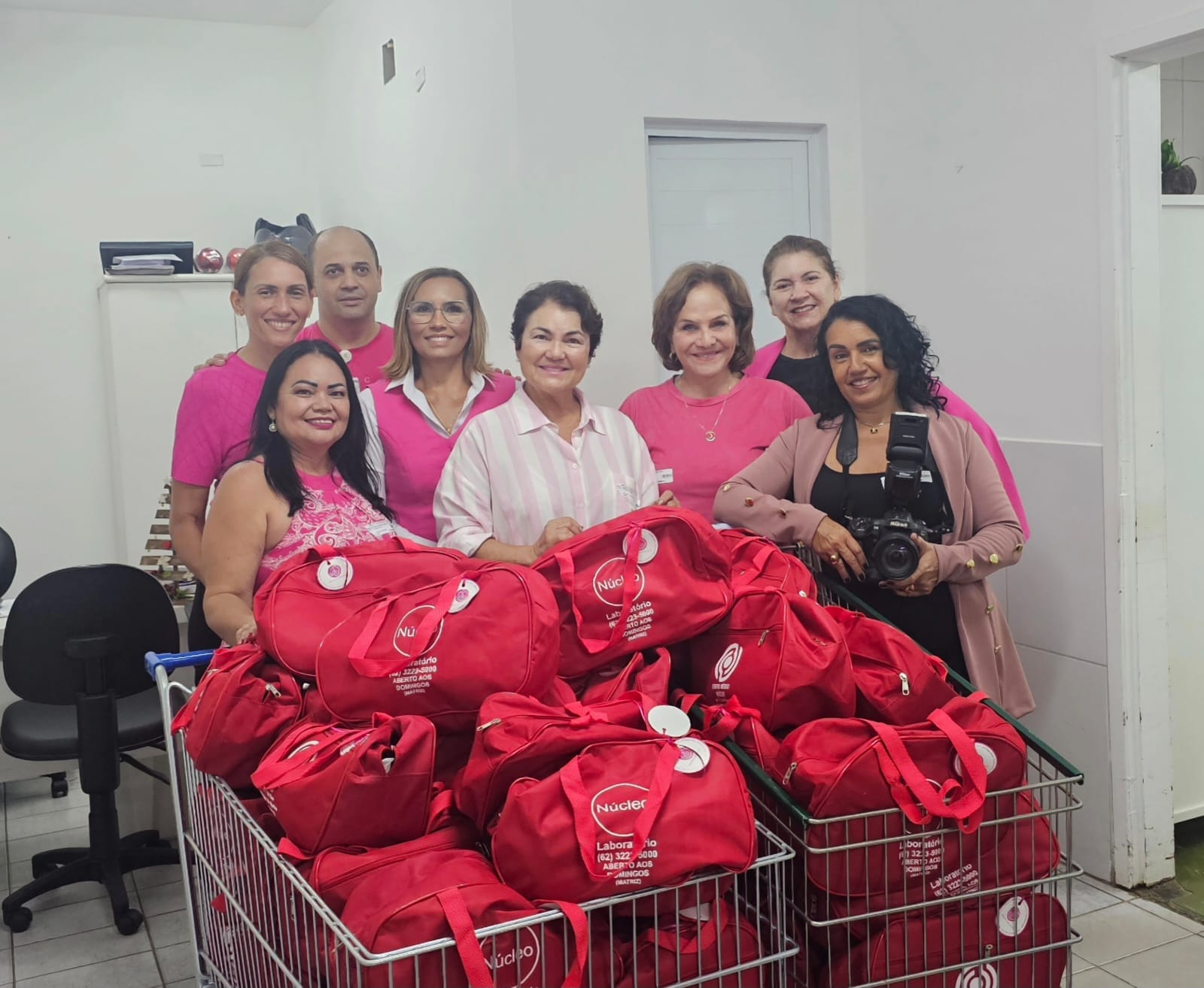 Mulheres e homem usando blusas rosas e preta com bolsa vermelhas.