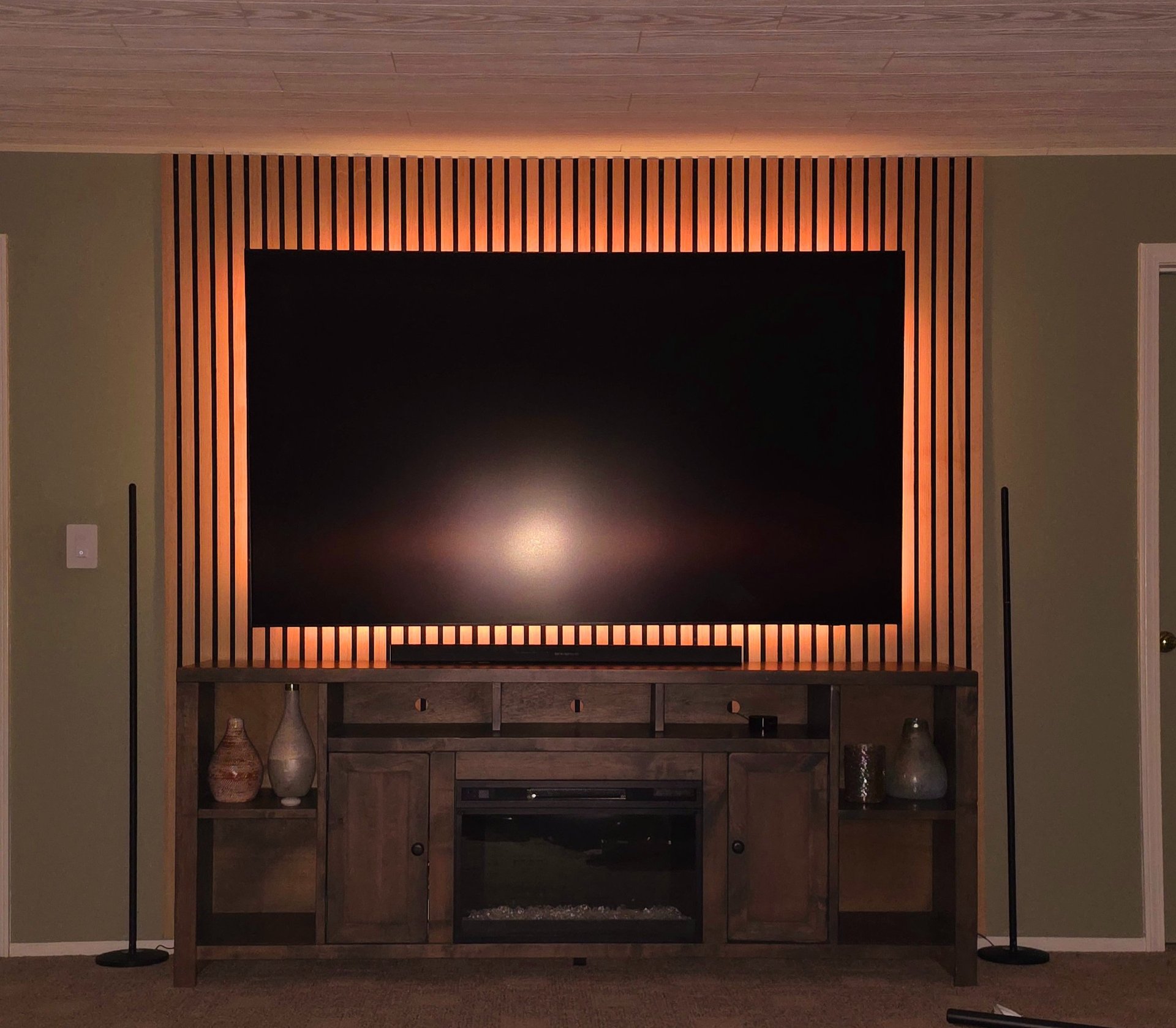 Modern home theater setup featuring a wall-mounted TV on a wood slat accent wall with LED backlight.