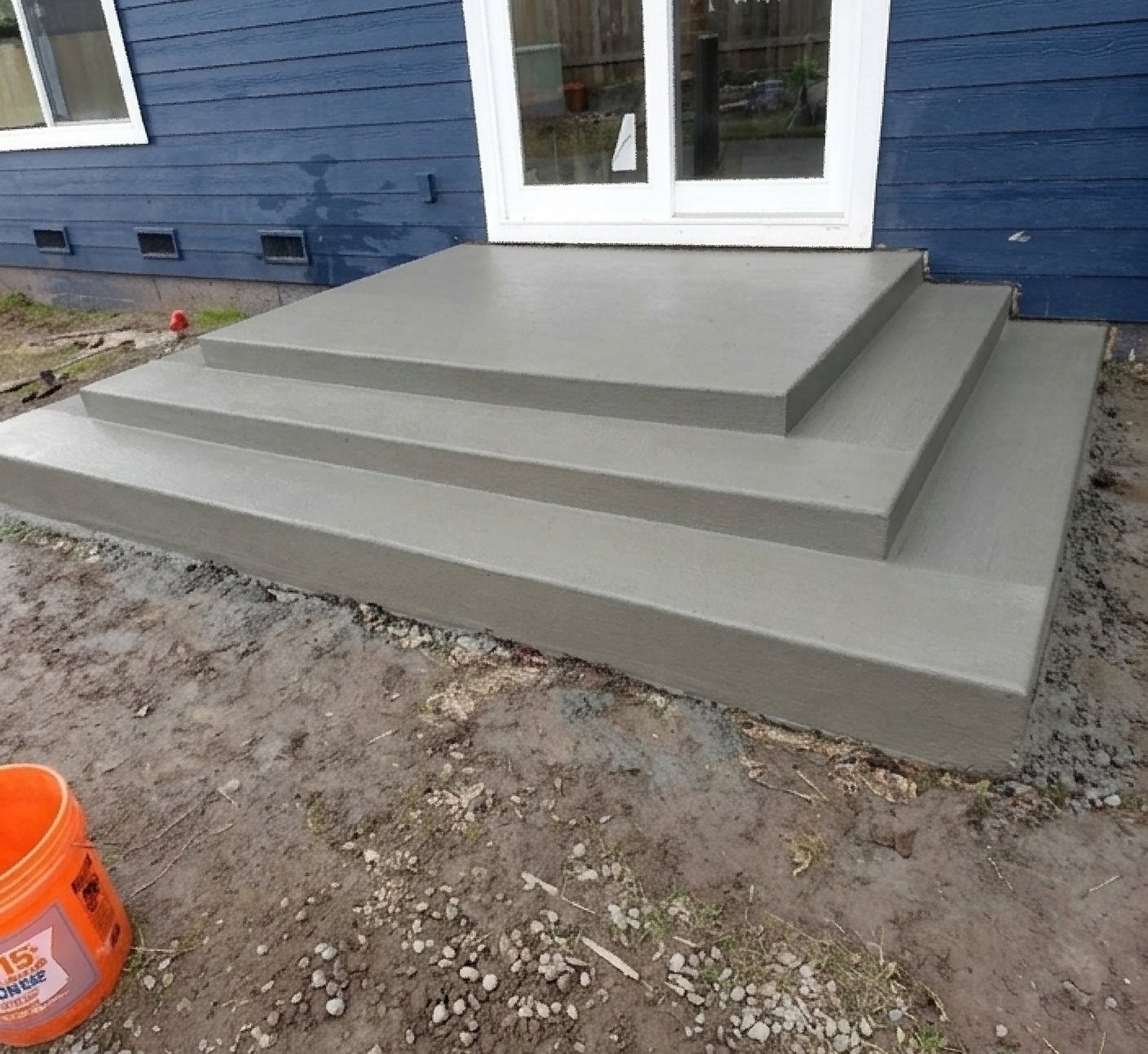 Newly poured concrete steps leading to a sliding glass door on a blue house, showcasing professional