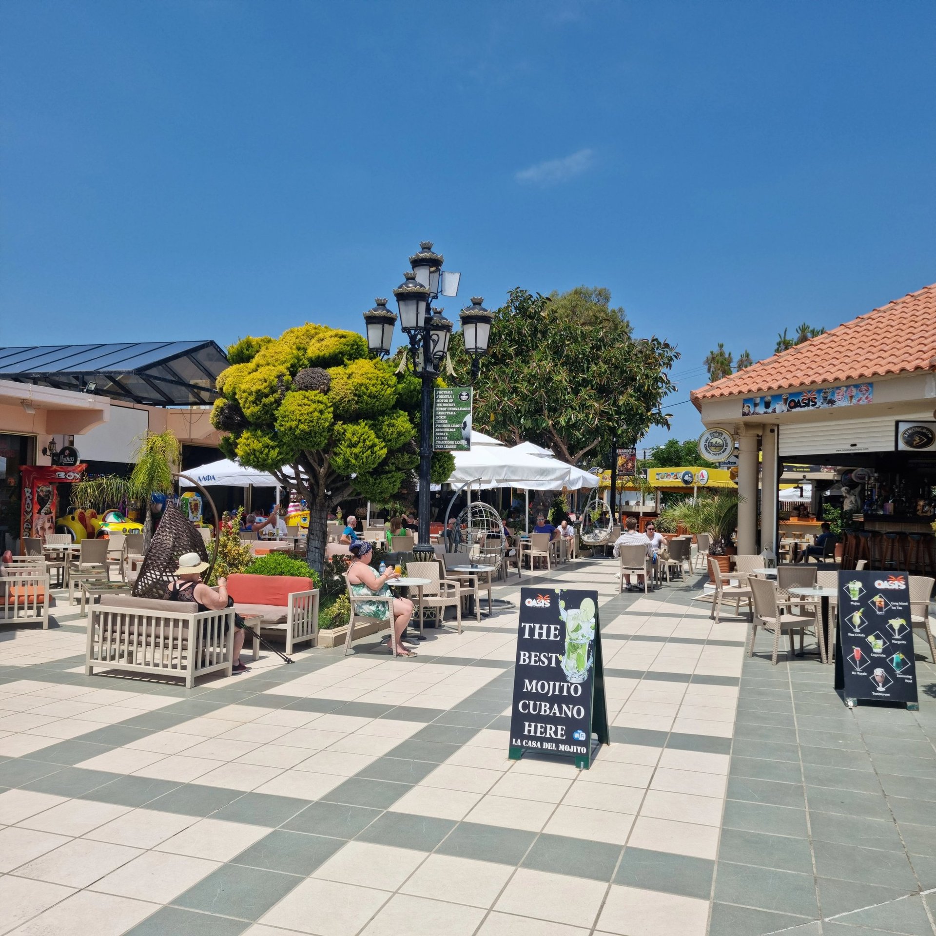 Sunny outdoor cafe patio with tourists enjoying drinks at a tropical vacation resort.