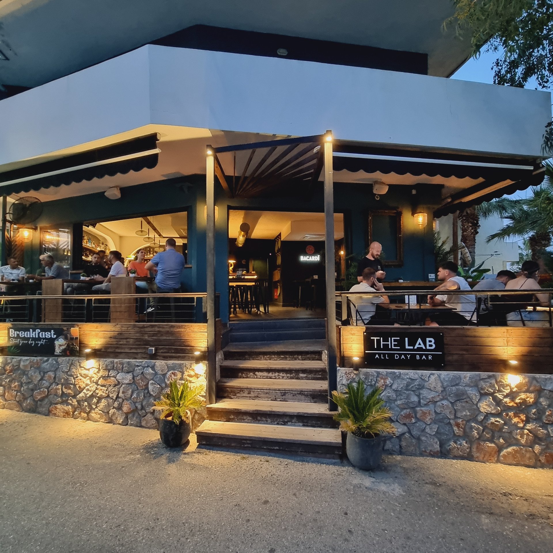 Customers dining at The Lab All Day Bar outdoor patio with stone walls and evening lighting.