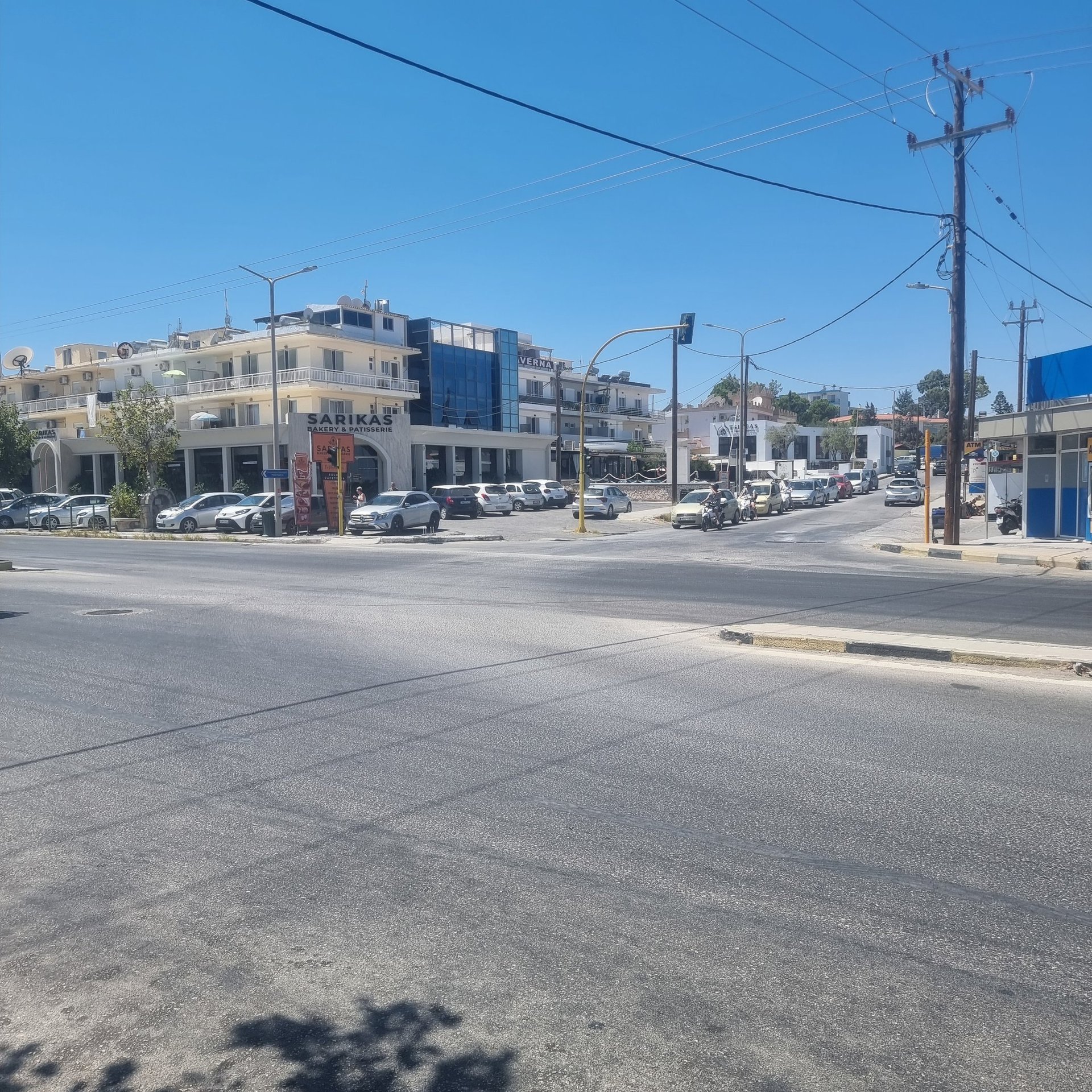 Sunny street intersection in Faliraki Rhodes with parked cars near the Sarikas building.