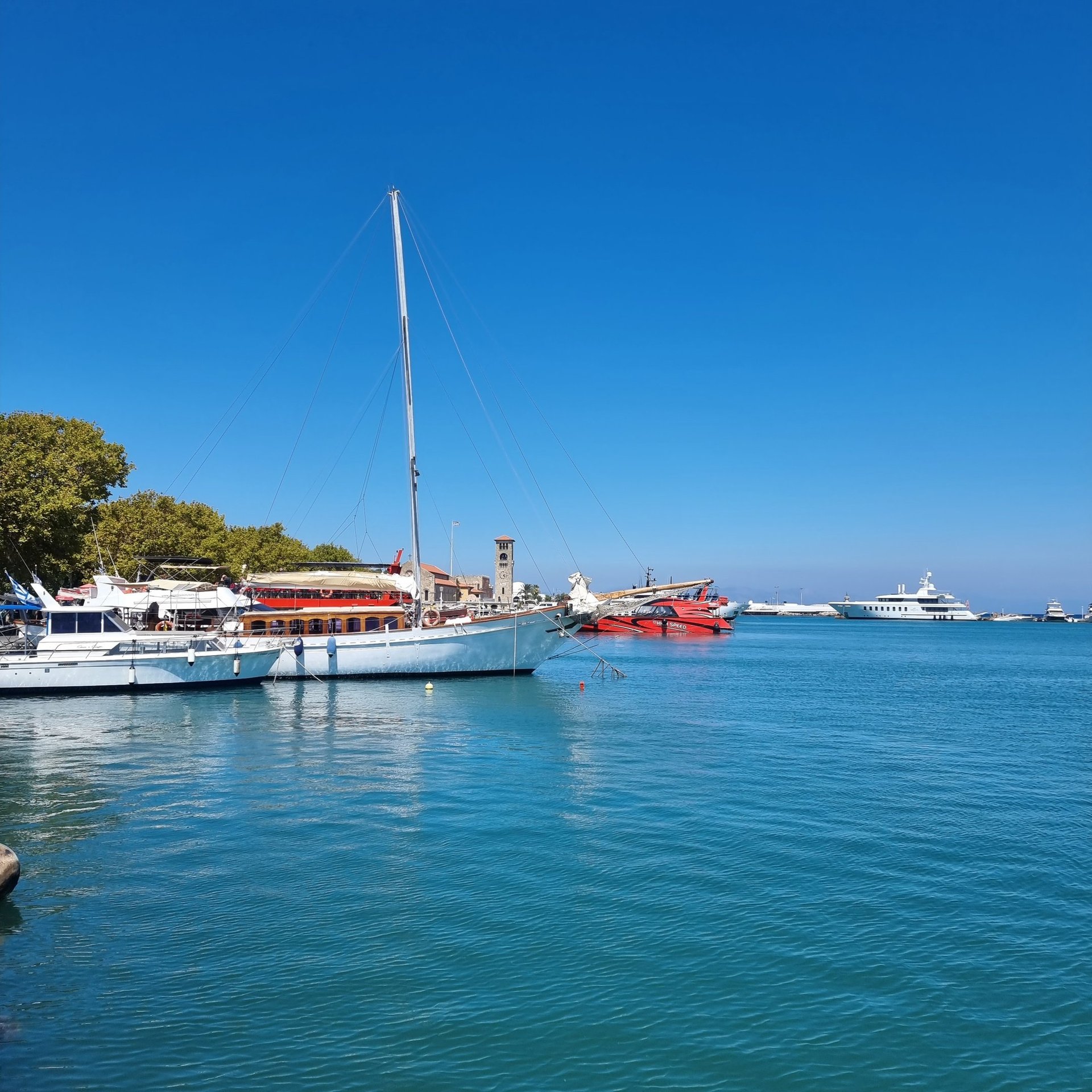 Luxury yachts and sailboats anchored in the sunny Mandraki Harbor of Rhodes, Greece.