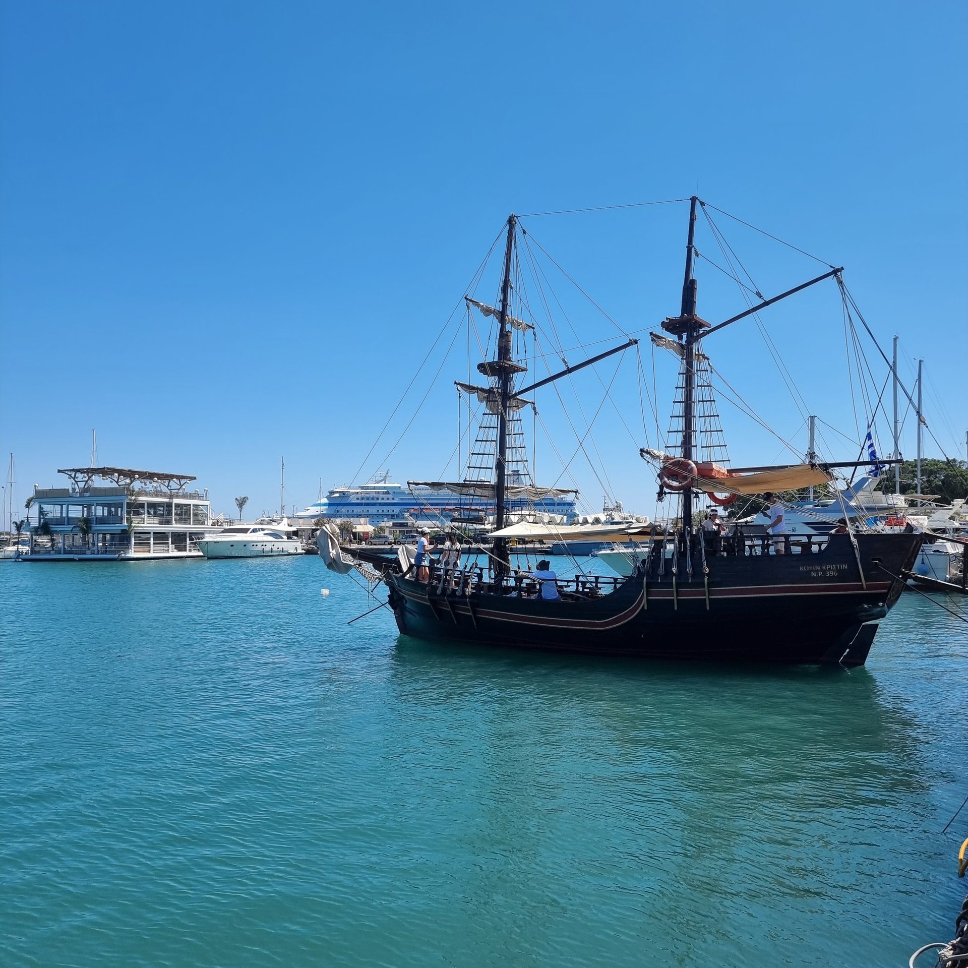 A vintage-style wooden pirate ship tour boat sailing in the blue waters of a Mediterranean harbor.