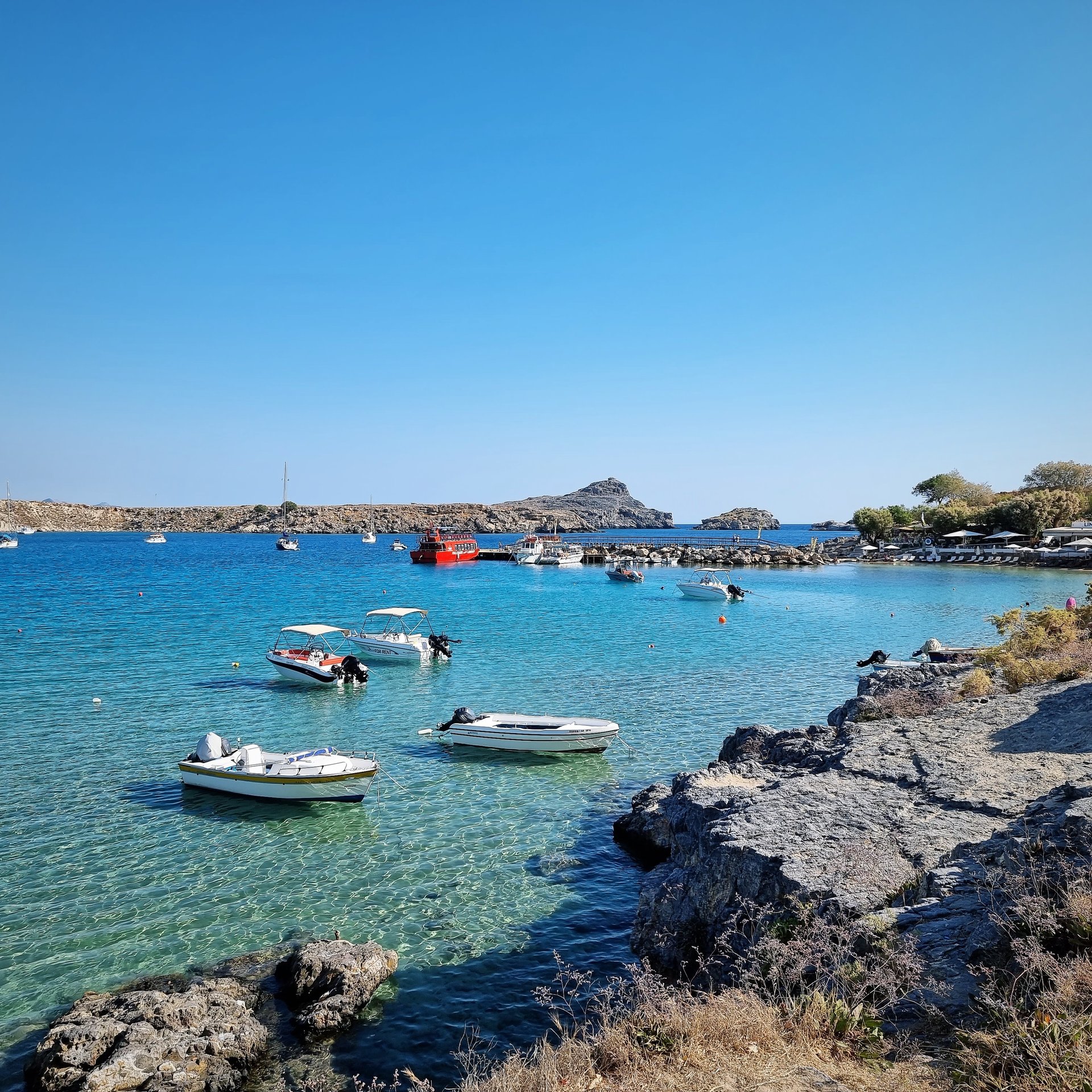 Scenic bay with crystal clear turquoise water, small boats, and a rocky coastline under a bright blue sky, ideal for summer