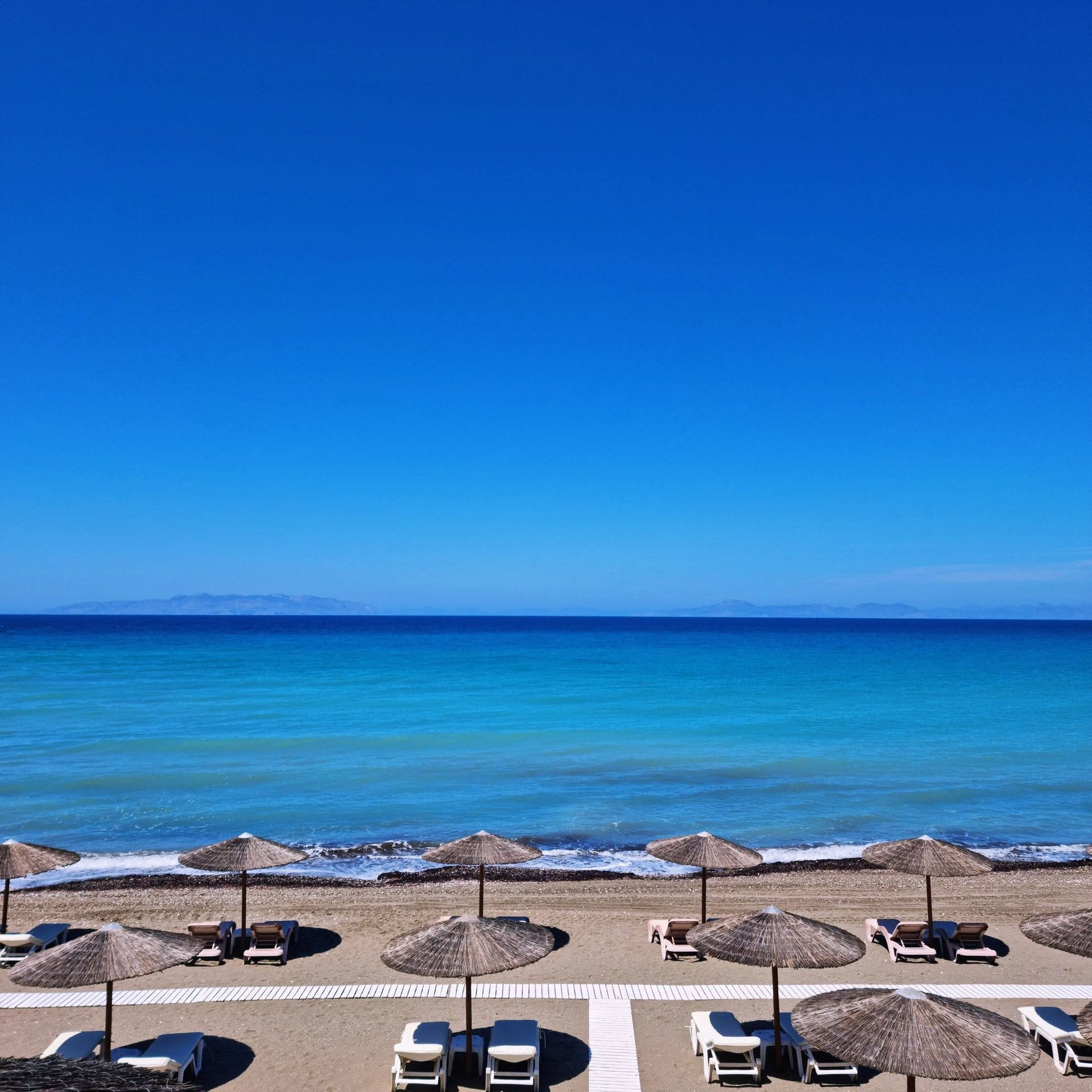 Luxury beach resort with thatched umbrellas and lounge chairs on a sandy shore by turquoise ocean water.