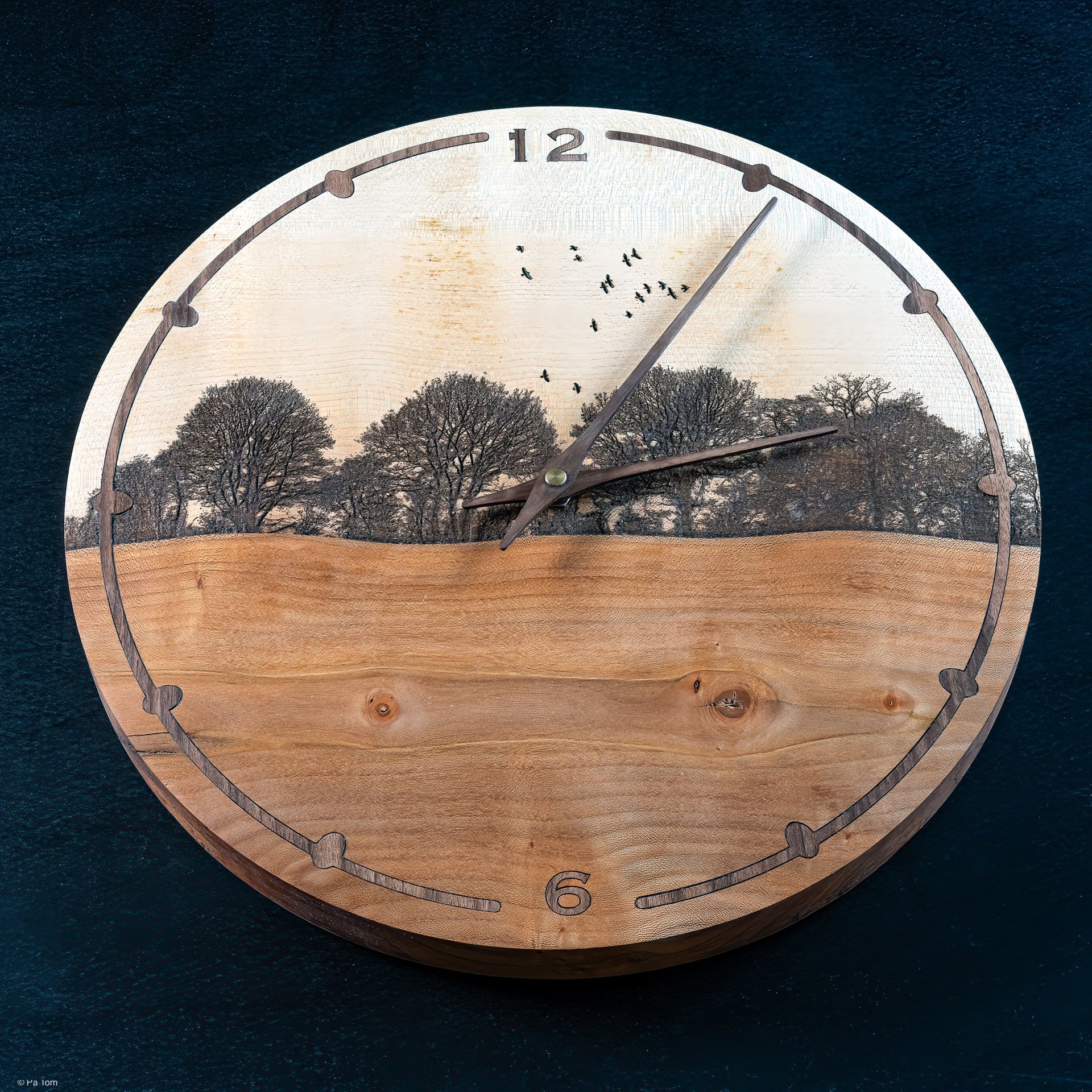Round wooden wall clock featuring an engraved nature landscape with trees and birds.