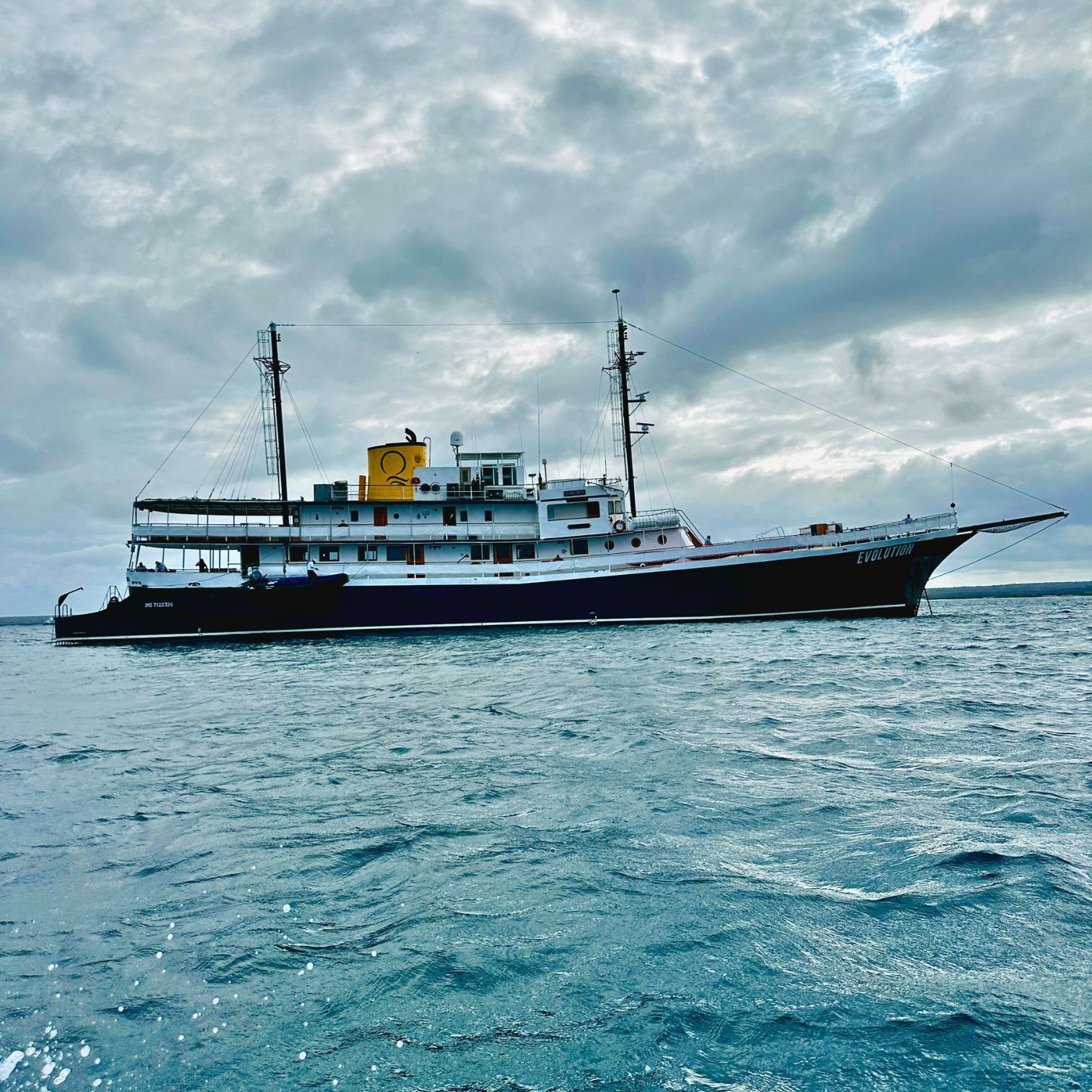 Luxury expedition yacht Evolution sailing on blue ocean water under a cloudy sky.