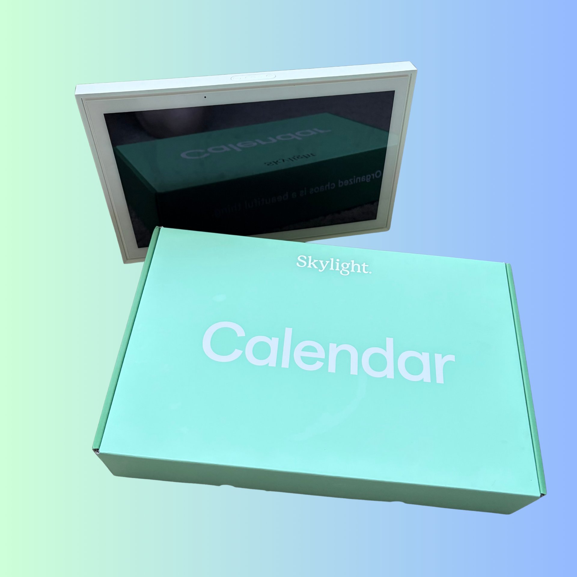 Skylight digital calendar smart display with its green retail packaging on a gradient background.