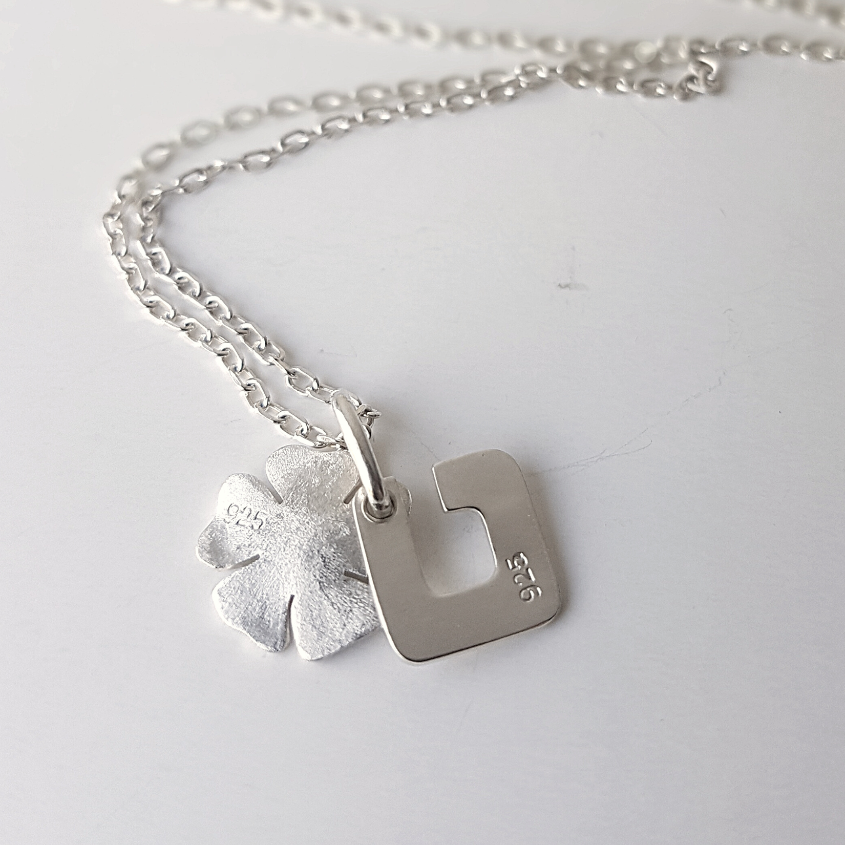 Sterling silver necklace with a four-leaf clover and square letter U charm, both stamped with 925 hallmarks.