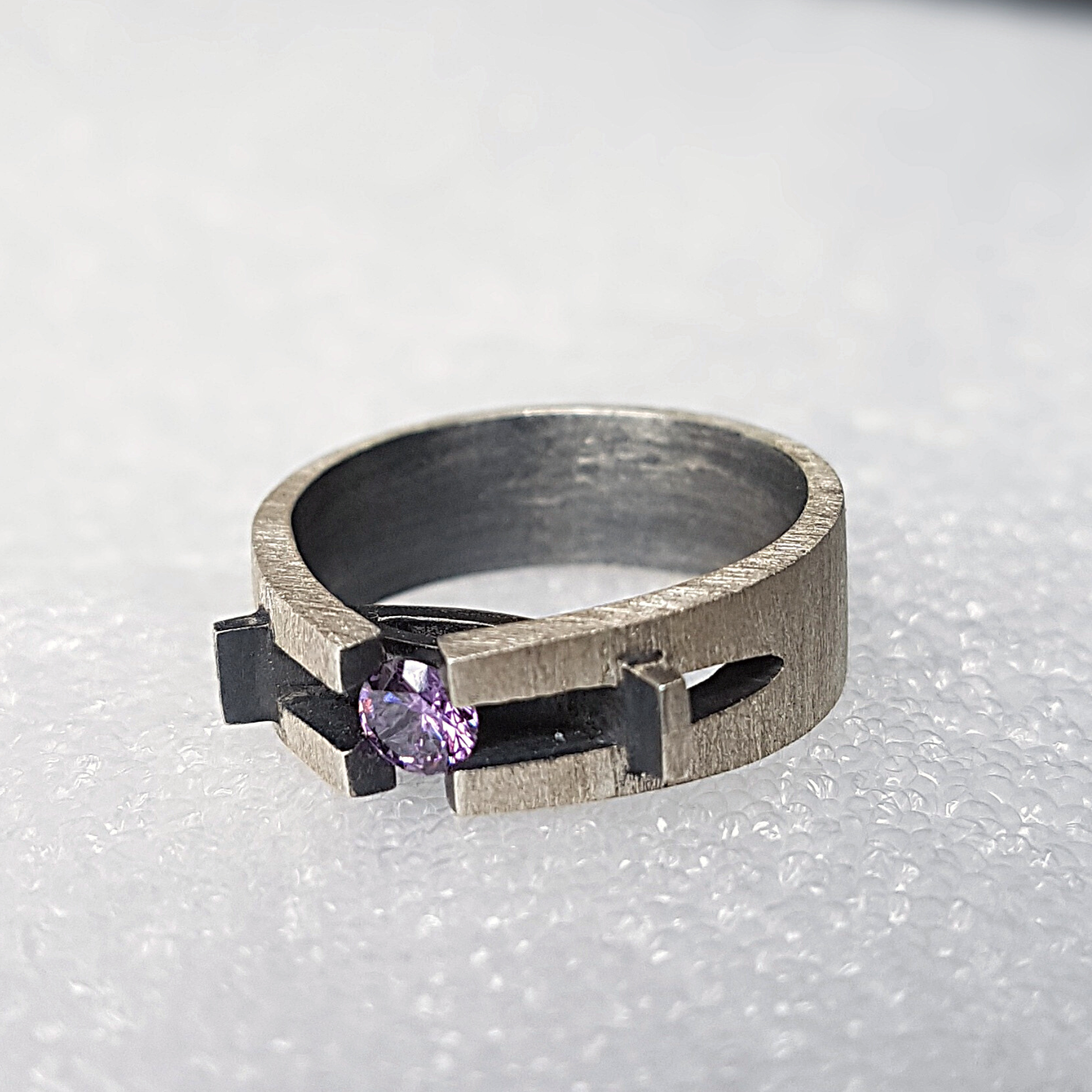 Handcrafted brushed silver ring featuring a round purple gemstone in a unique architectural setting.