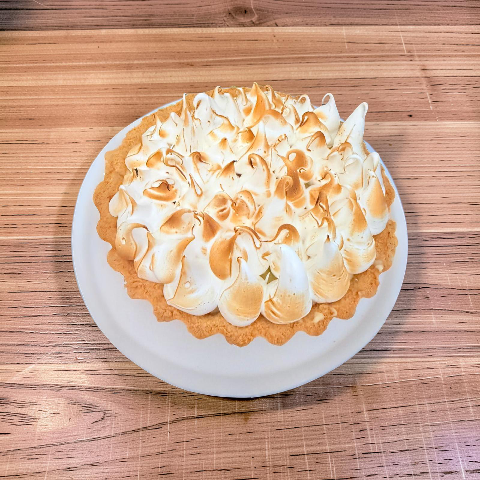 Una tarta casera de merengue de limón con picos tostados en un plato blanco sobre una mesa de madera