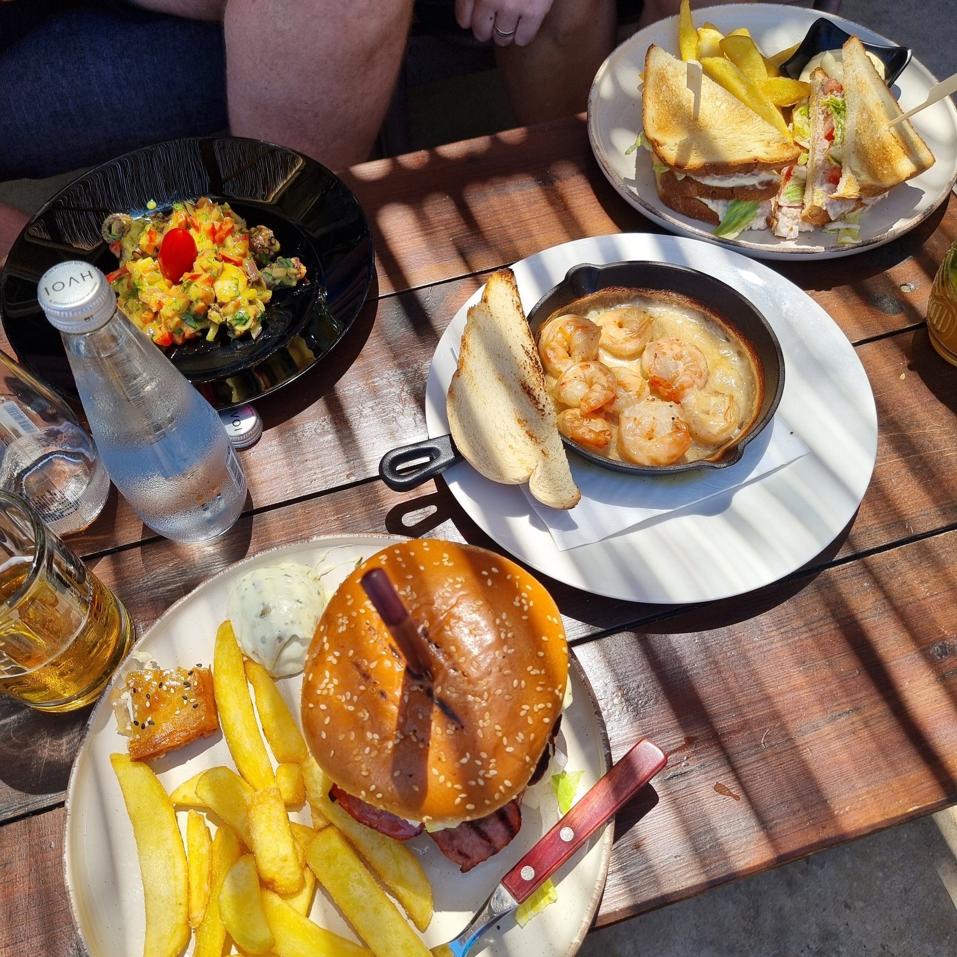Gourmet lunch spread featuring a cheeseburger with fries, garlic shrimp in a skillet, and a club sandwich.