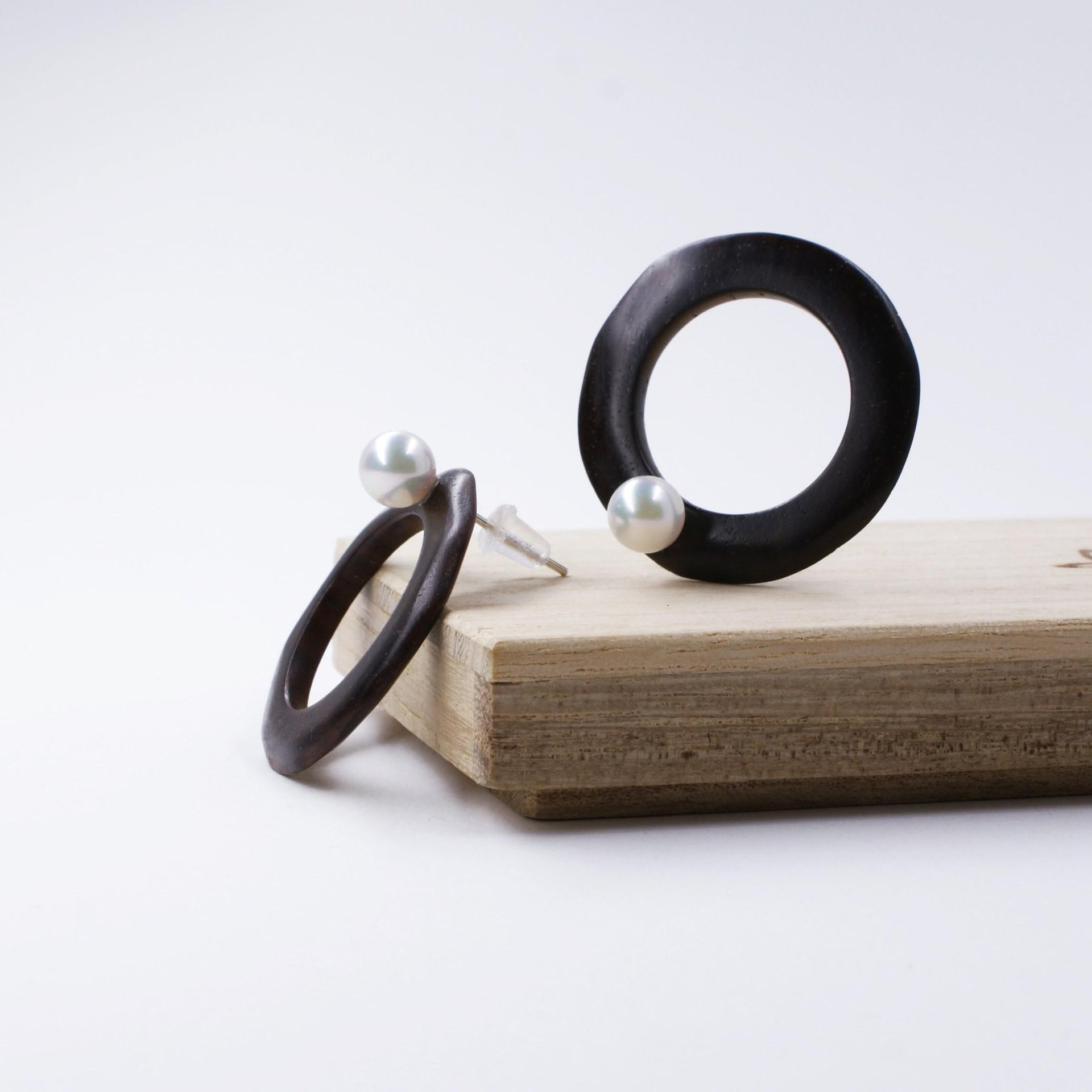 Handmade black ebony wood hoop earrings with white pearls displayed on a wooden block.