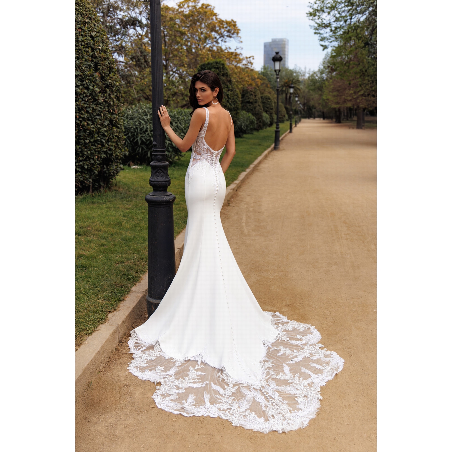 Elegant backless mermaid wedding dress with a long lace train on a park path.