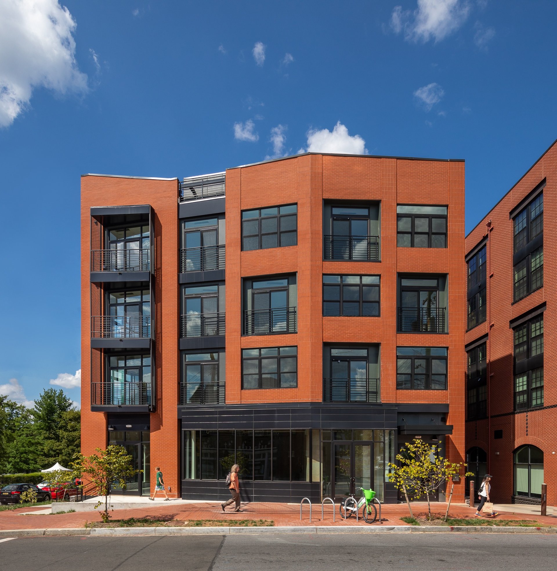 Modern red brick apartment building with black window frames and private balconies under a blue sky.