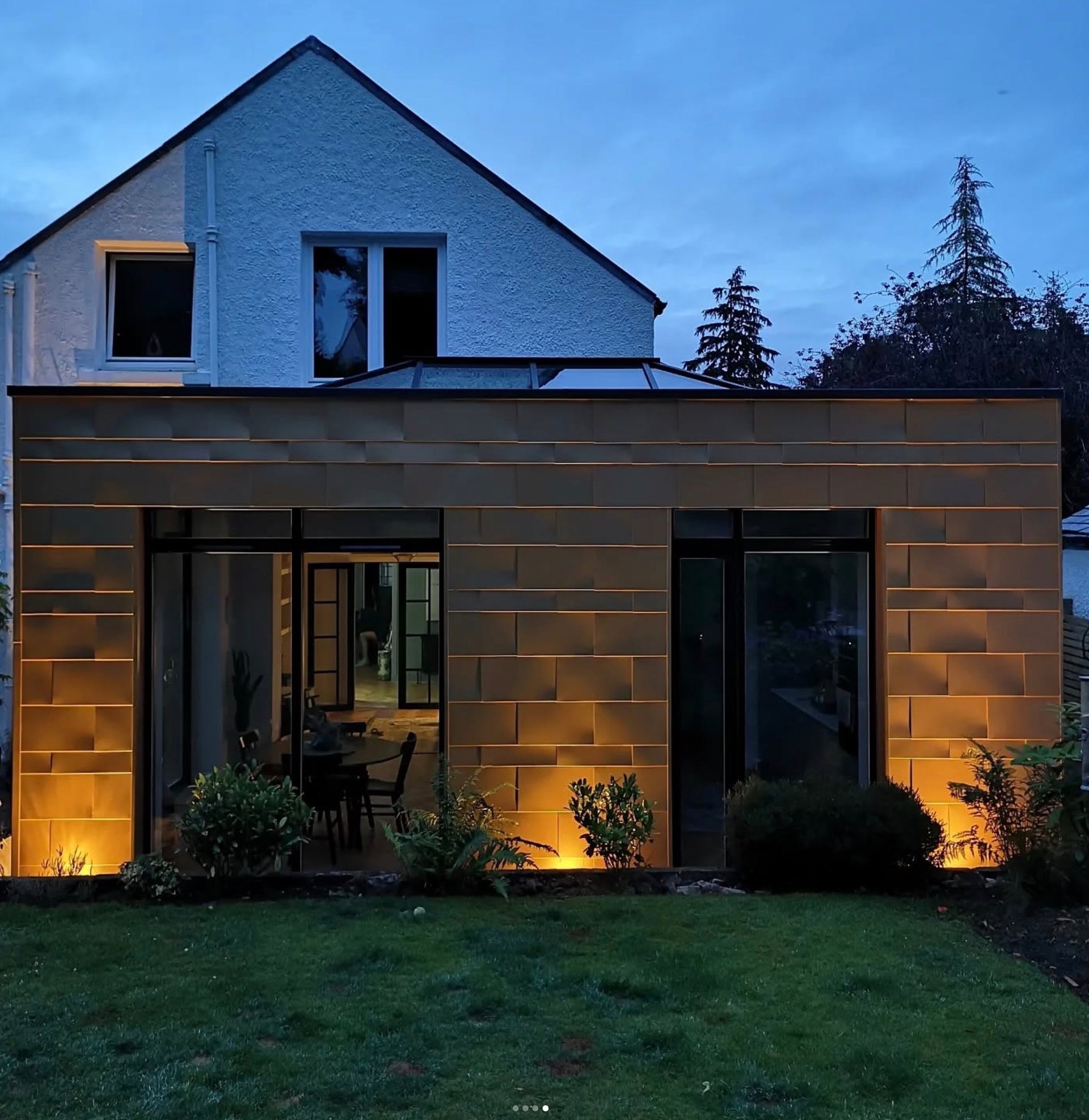 Modern copper-clad home extension with integrated outdoor lighting and large glass sliding doors.