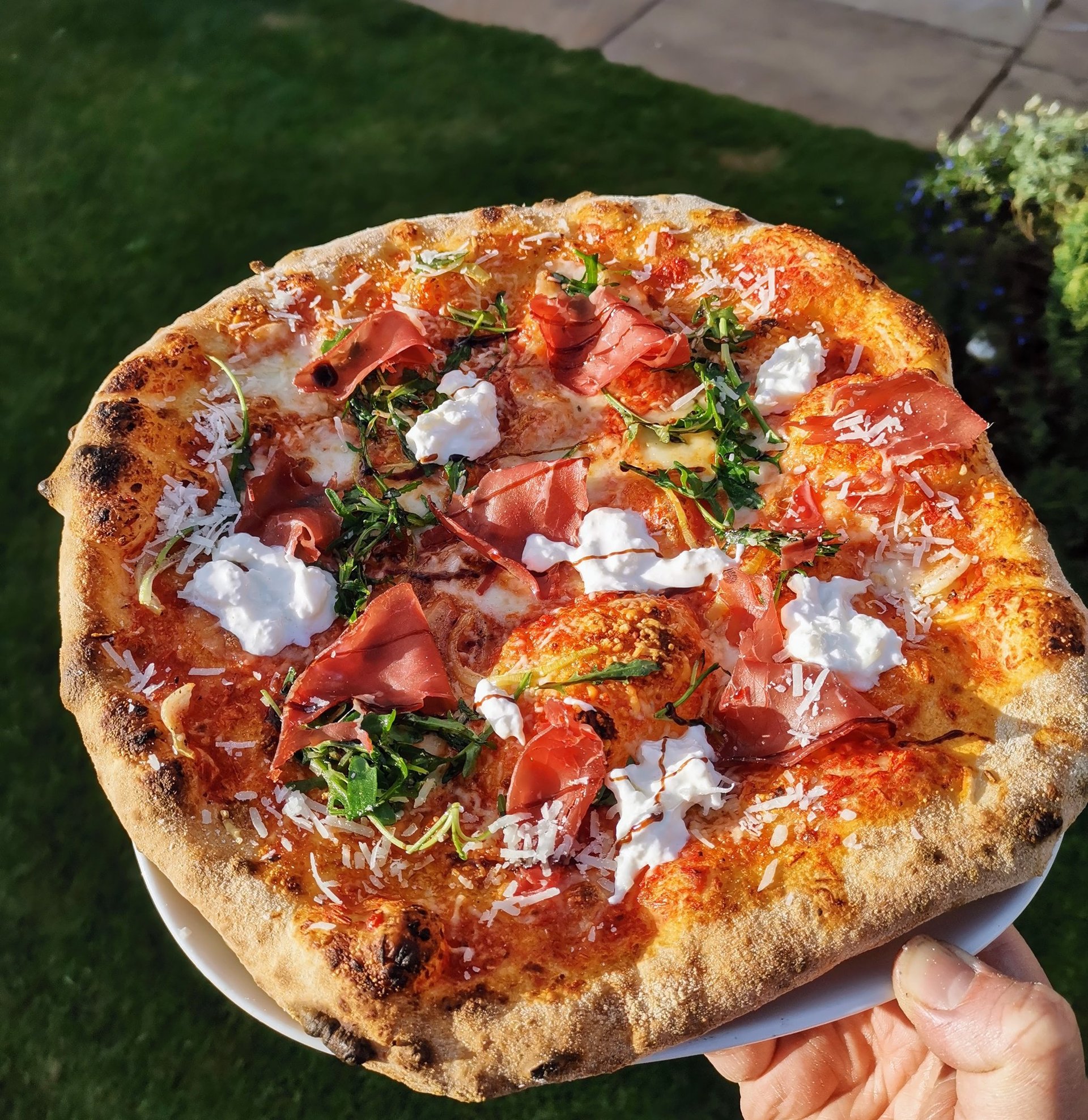 Handmade Neapolitan pizza with prosciutto, burrata cheese, and arugula over a crispy sourdough crust.